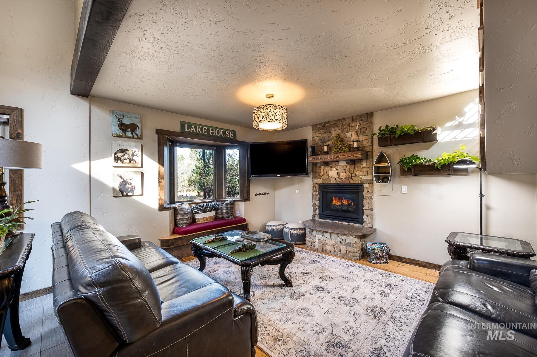 Living room with a textured ceiling, a stone fireplace, and wood finished floors