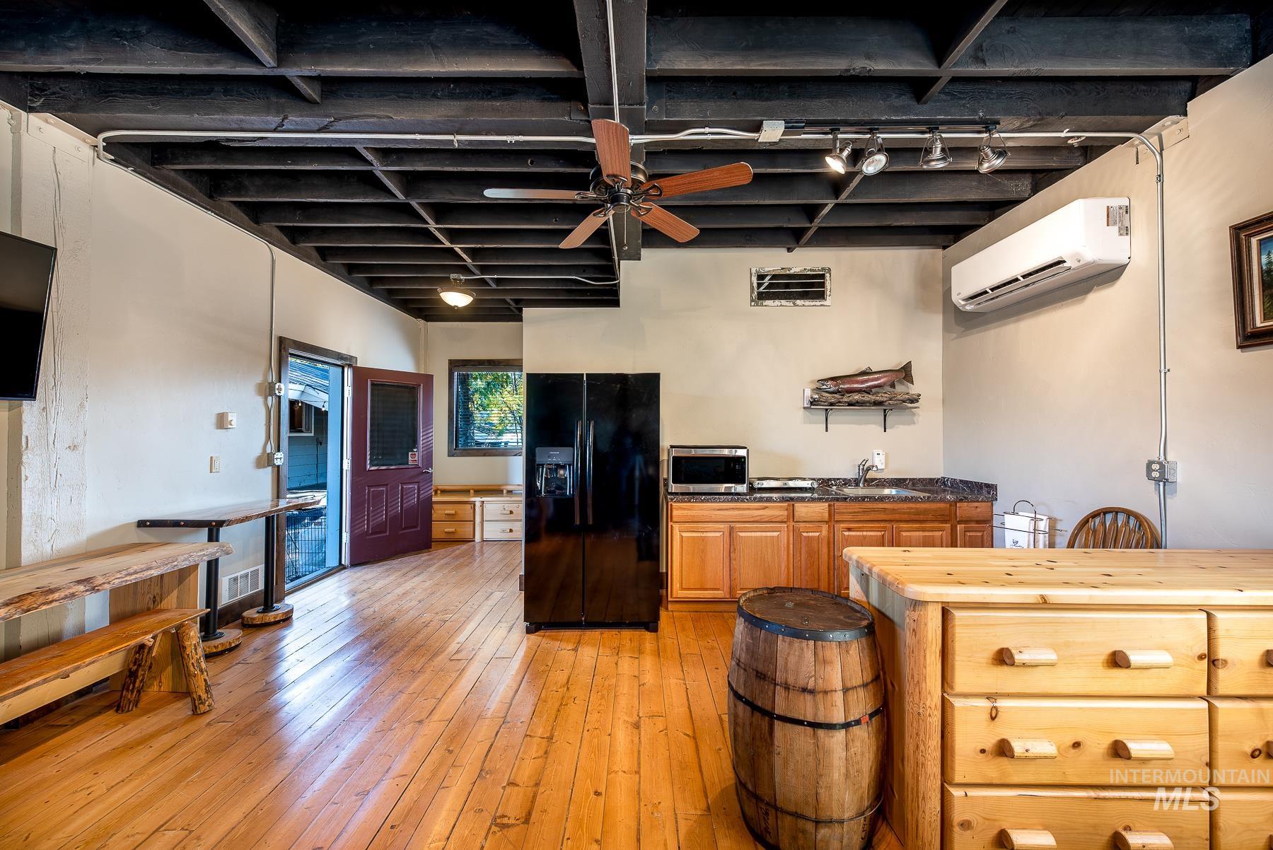 Kitchen with a ceiling fan, black fridge, light wood-type flooring, stainless steel microwave, and track lighting