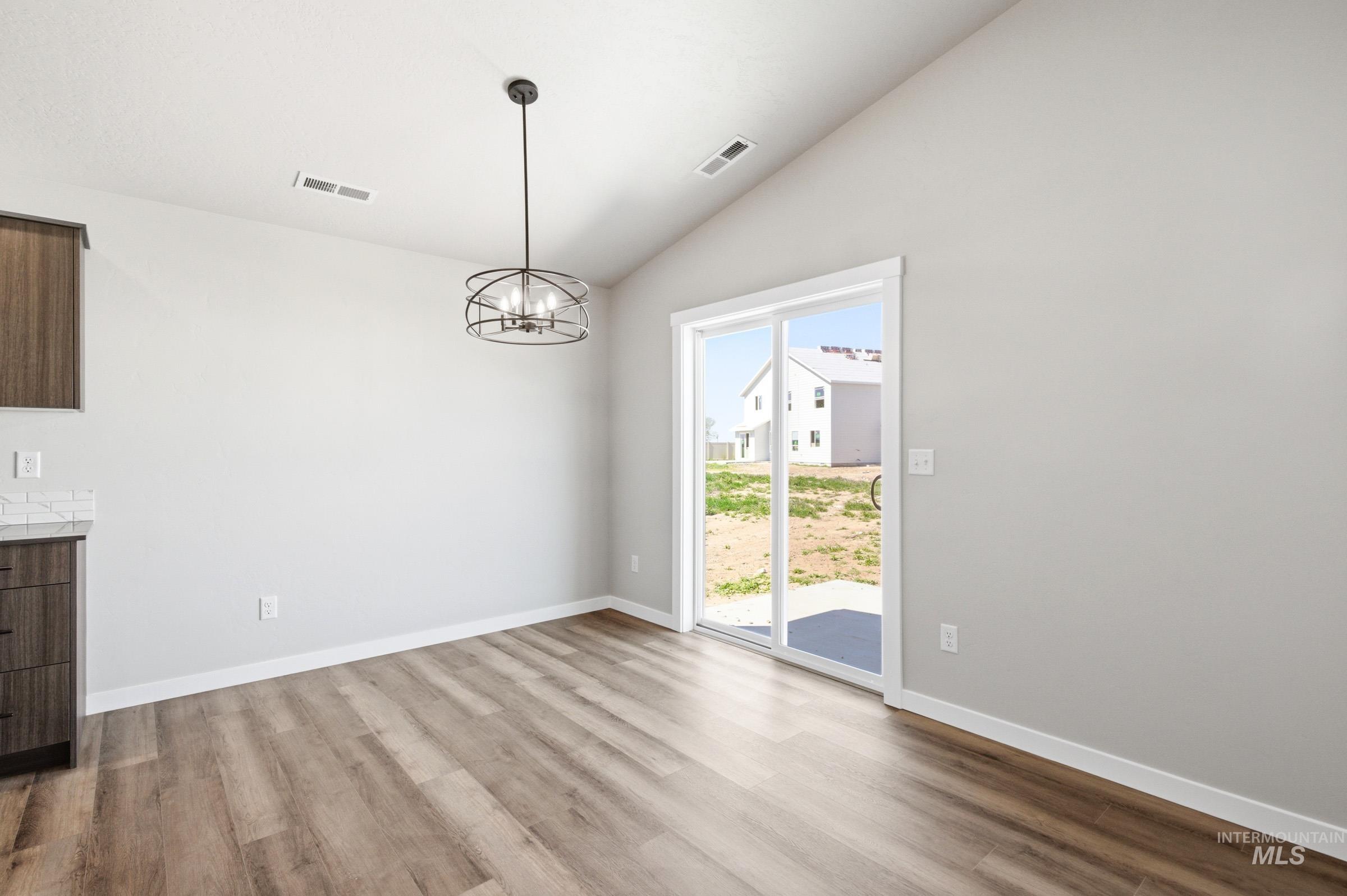 Dining area featuring wood-finish flooring, a contemporary chandelier, and vaulted ceilings