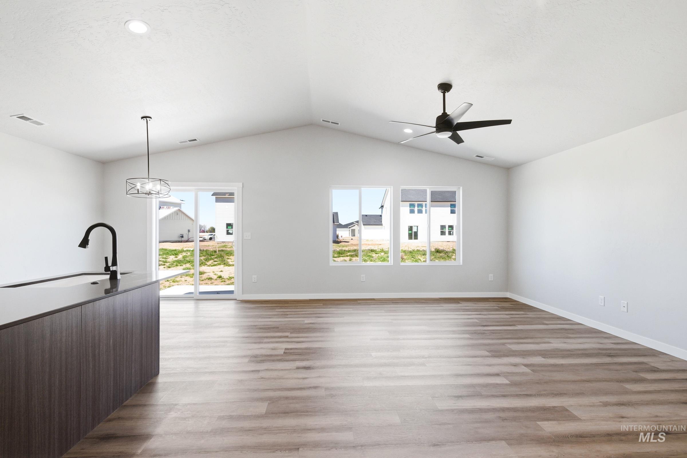 Open-concept living space featuring vaulted ceilings, wood-finish flooring, and ample natural light from multiple windows