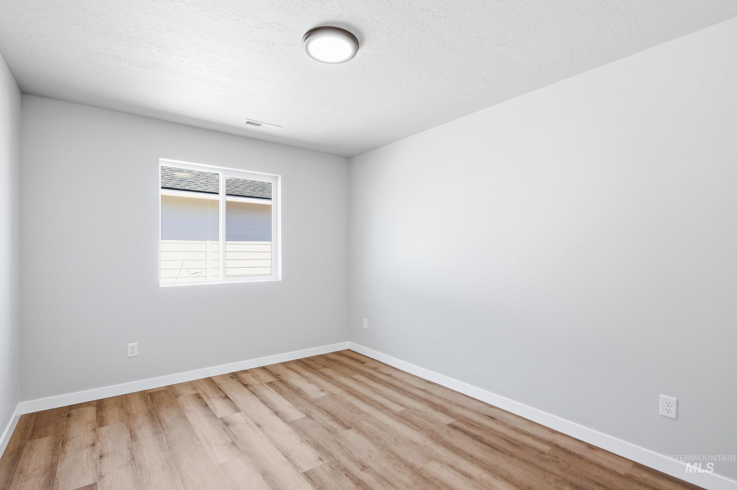 Room featuring wood-finish flooring, crisp white baseboards, and light gray walls