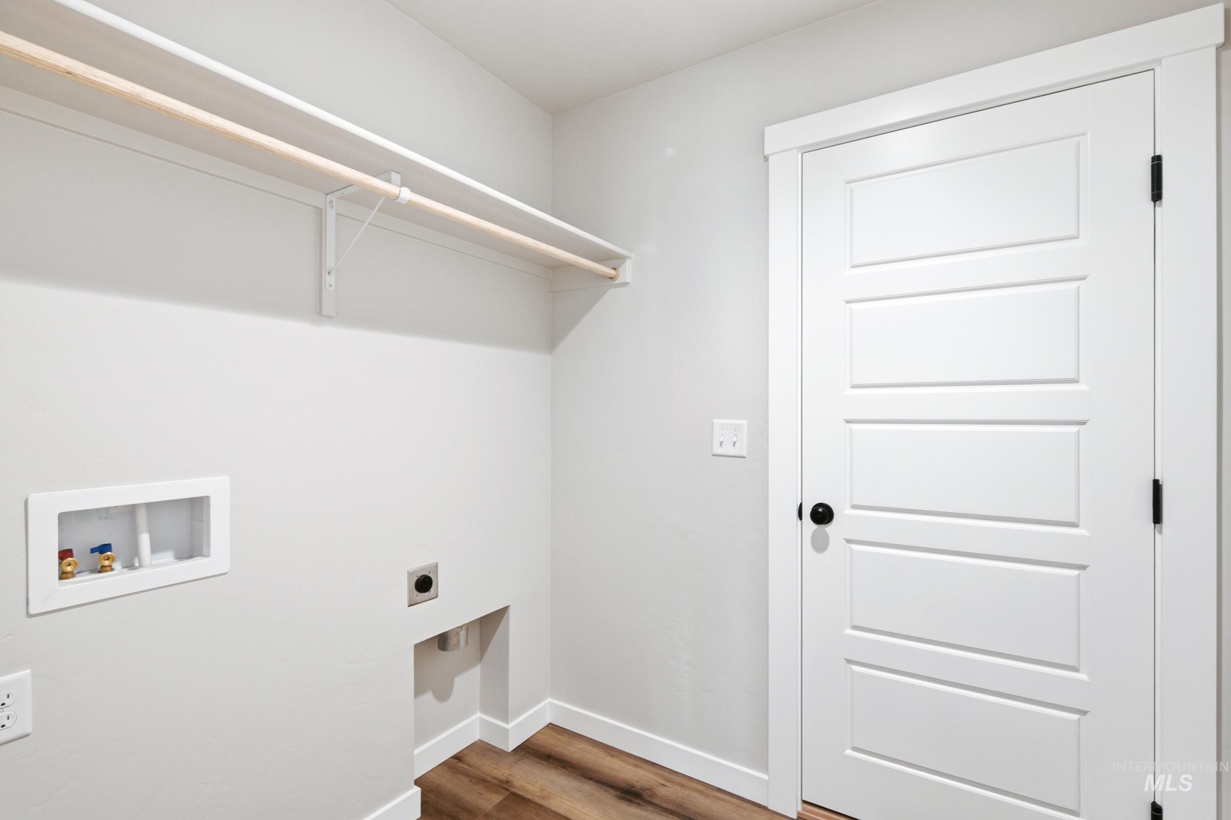 Dedicated laundry area featuring wood-finish flooring and a white five-panel interior door