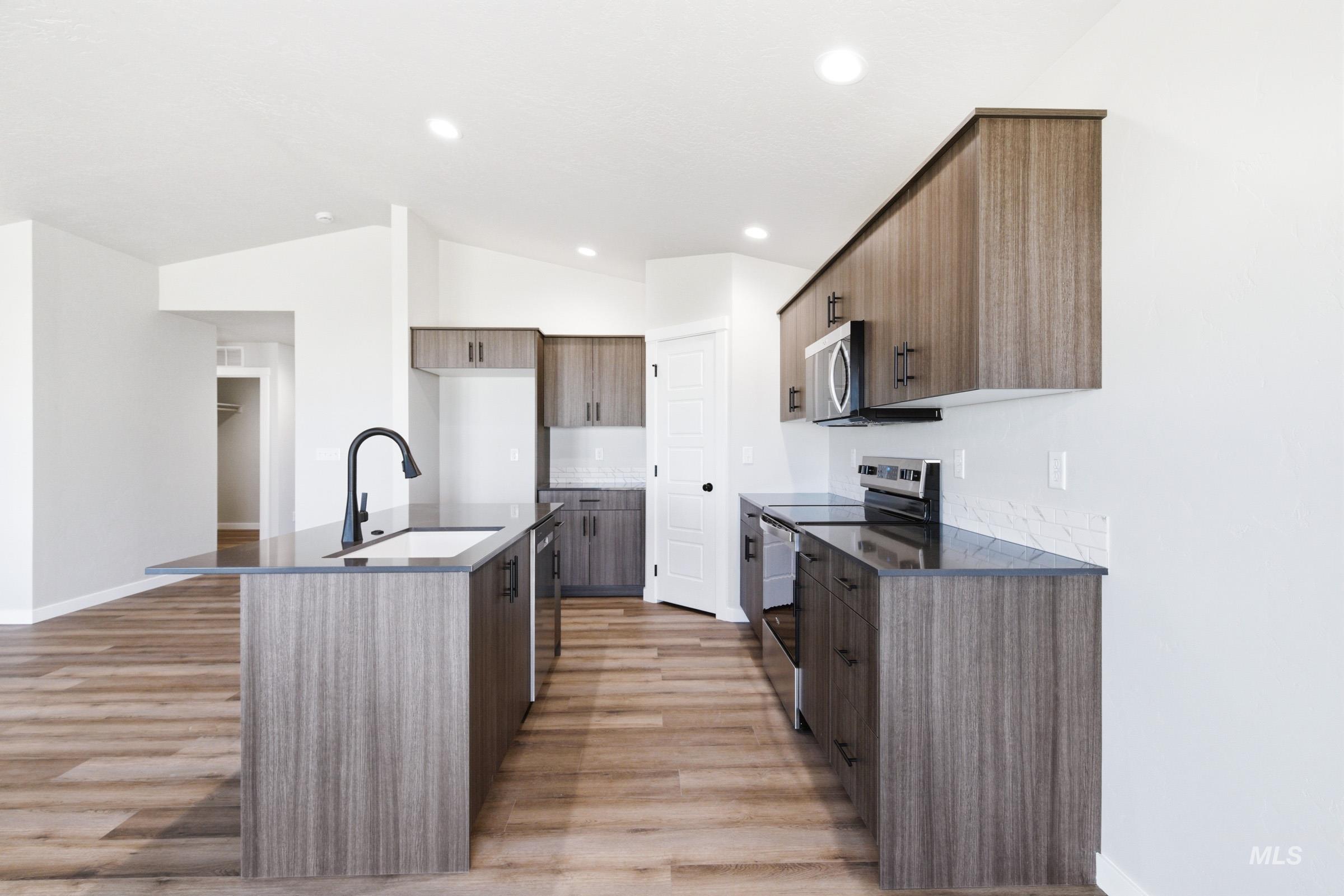 Kitchen featuring wood-finish cabinetry, dark countertops, a stainless steel appliance suite, and wood-finish flooring