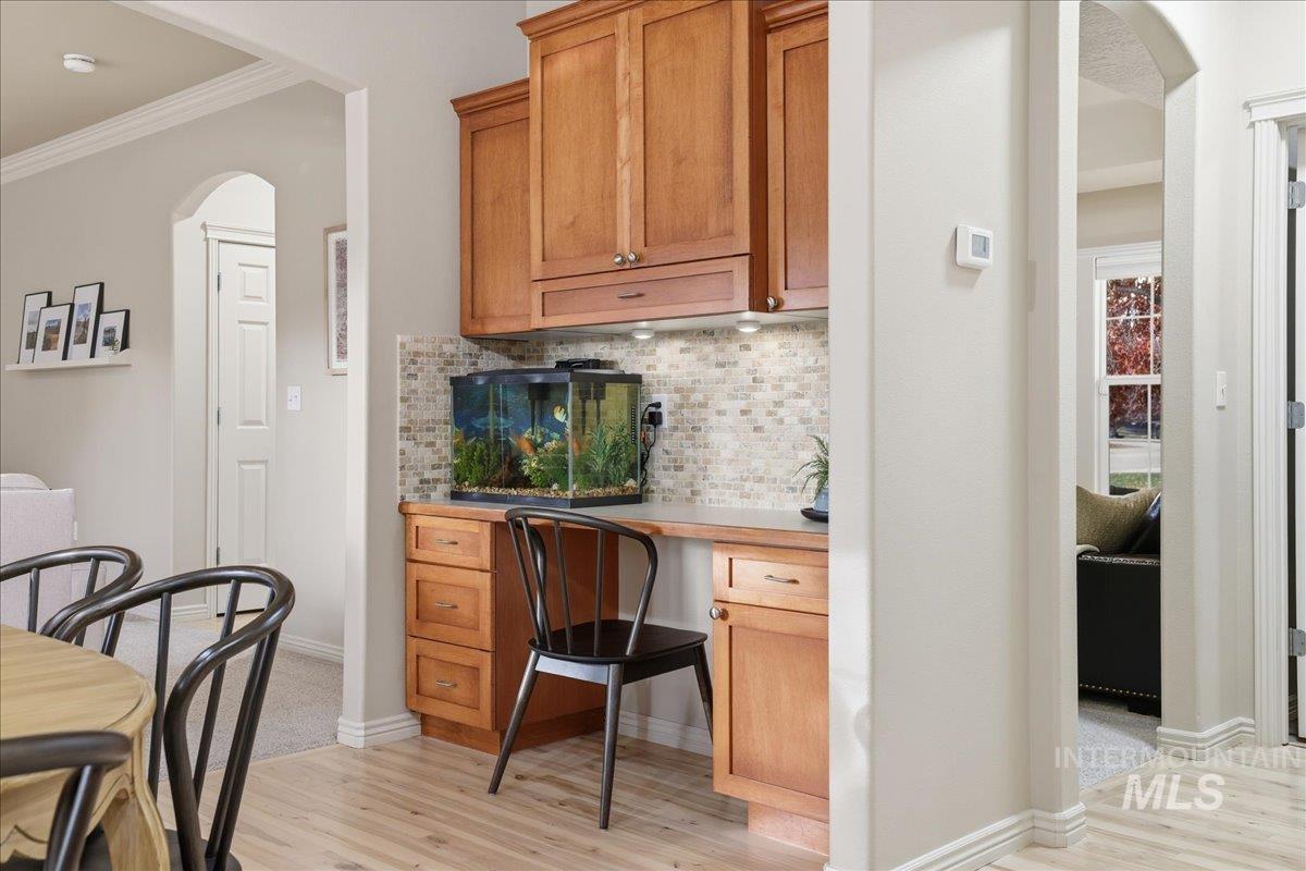 Bar featuring arched walkways, light wood-style floors, decorative backsplash, ornamental molding, and light countertops