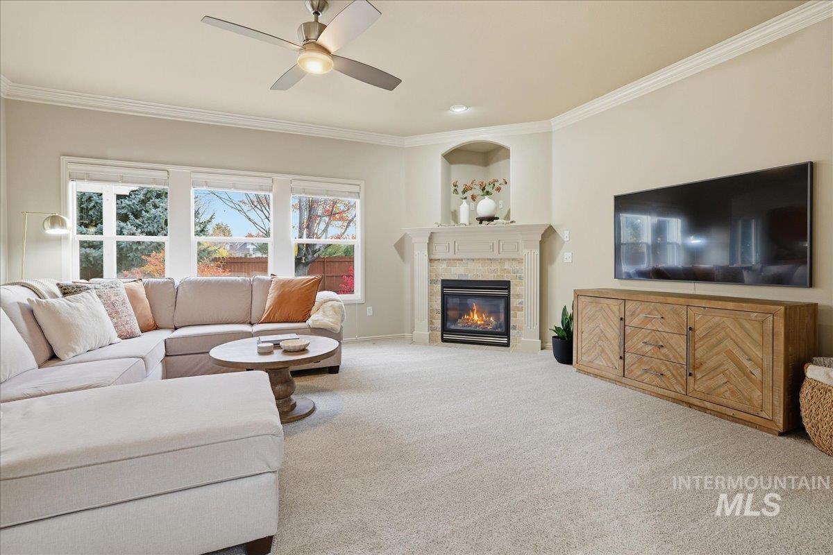 Living area featuring carpet, crown molding, a tiled fireplace, and ceiling fan