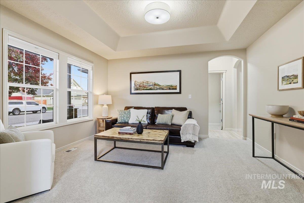 Living area featuring a tray ceiling, carpet flooring, arched walkways, and a textured ceiling