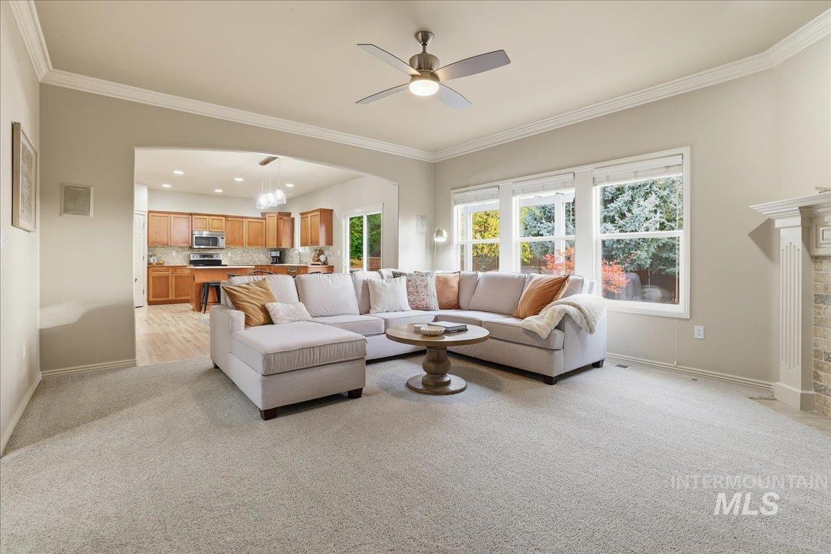Living area with light carpet, a chandelier, ornamental molding, and ceiling fan