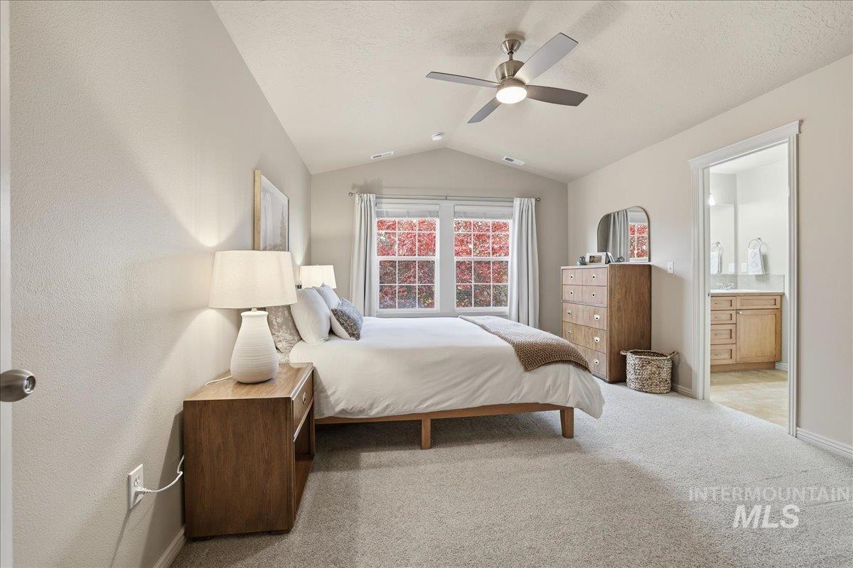 Bedroom featuring light carpet, vaulted ceiling, ensuite bathroom, a ceiling fan, and a textured ceiling