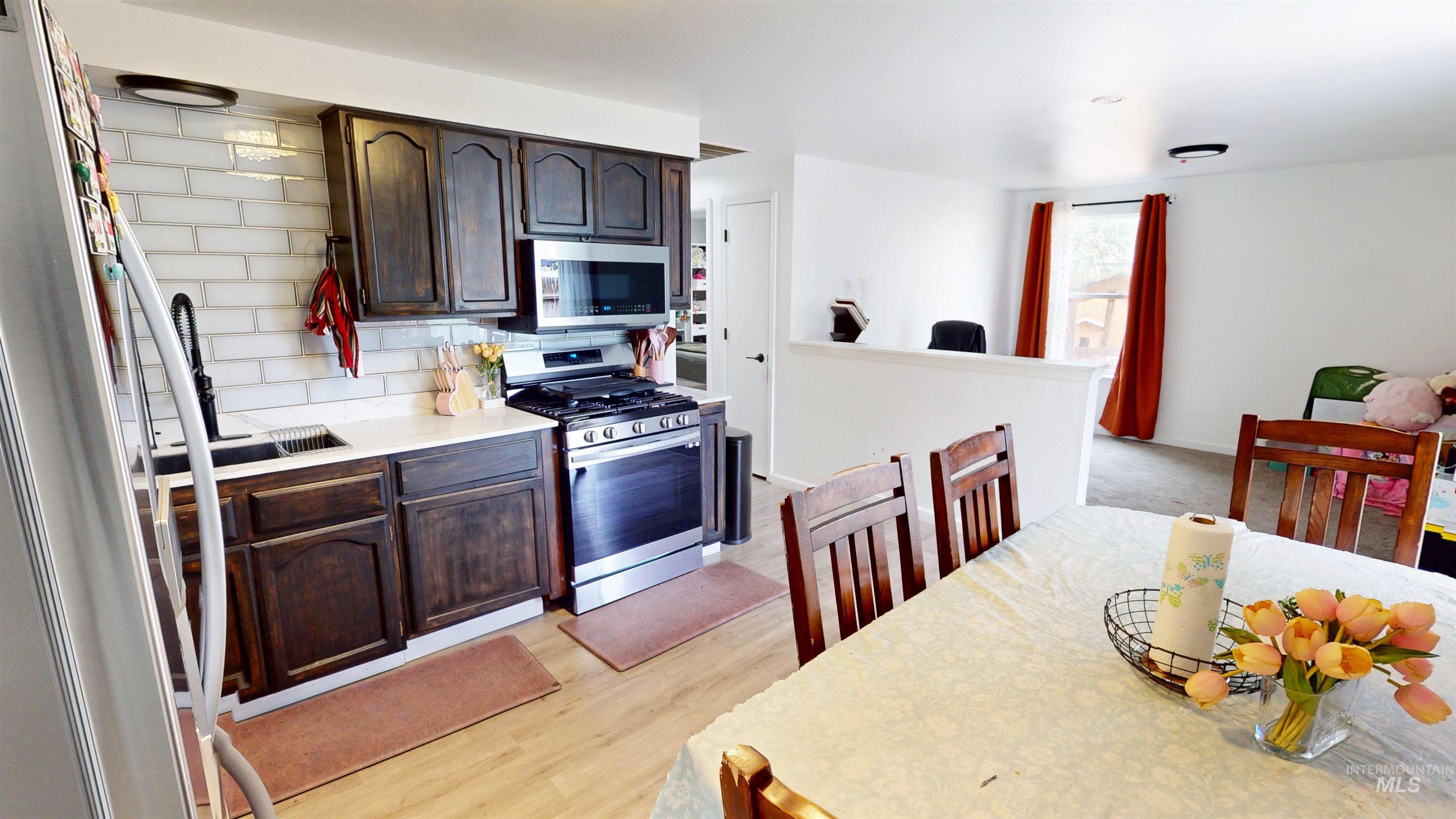 Kitchen with appliances with stainless steel finishes, dark brown cabinetry, backsplash, and light wood-style flooring