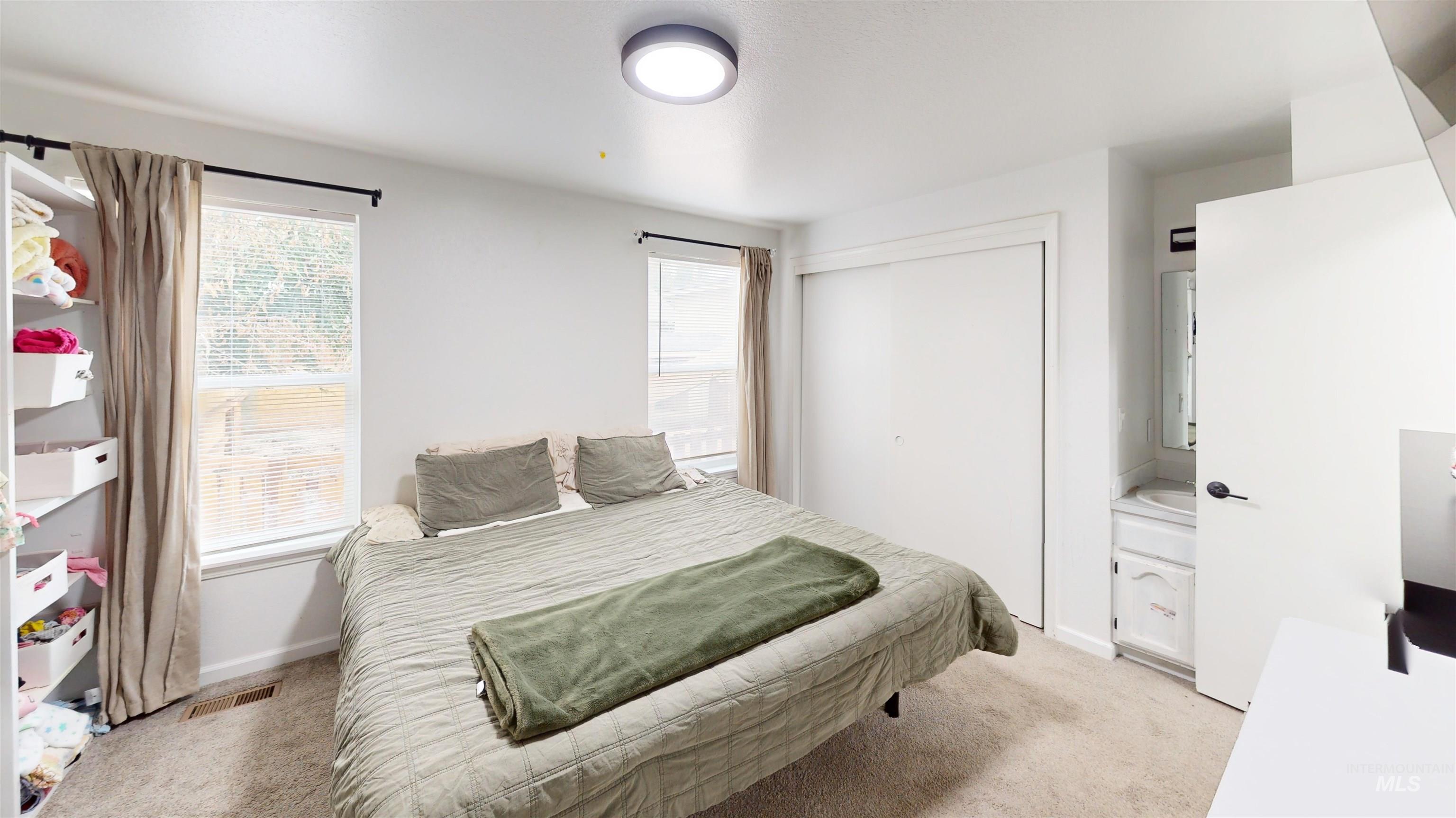 Bedroom featuring light colored carpet, multiple windows, and a closet