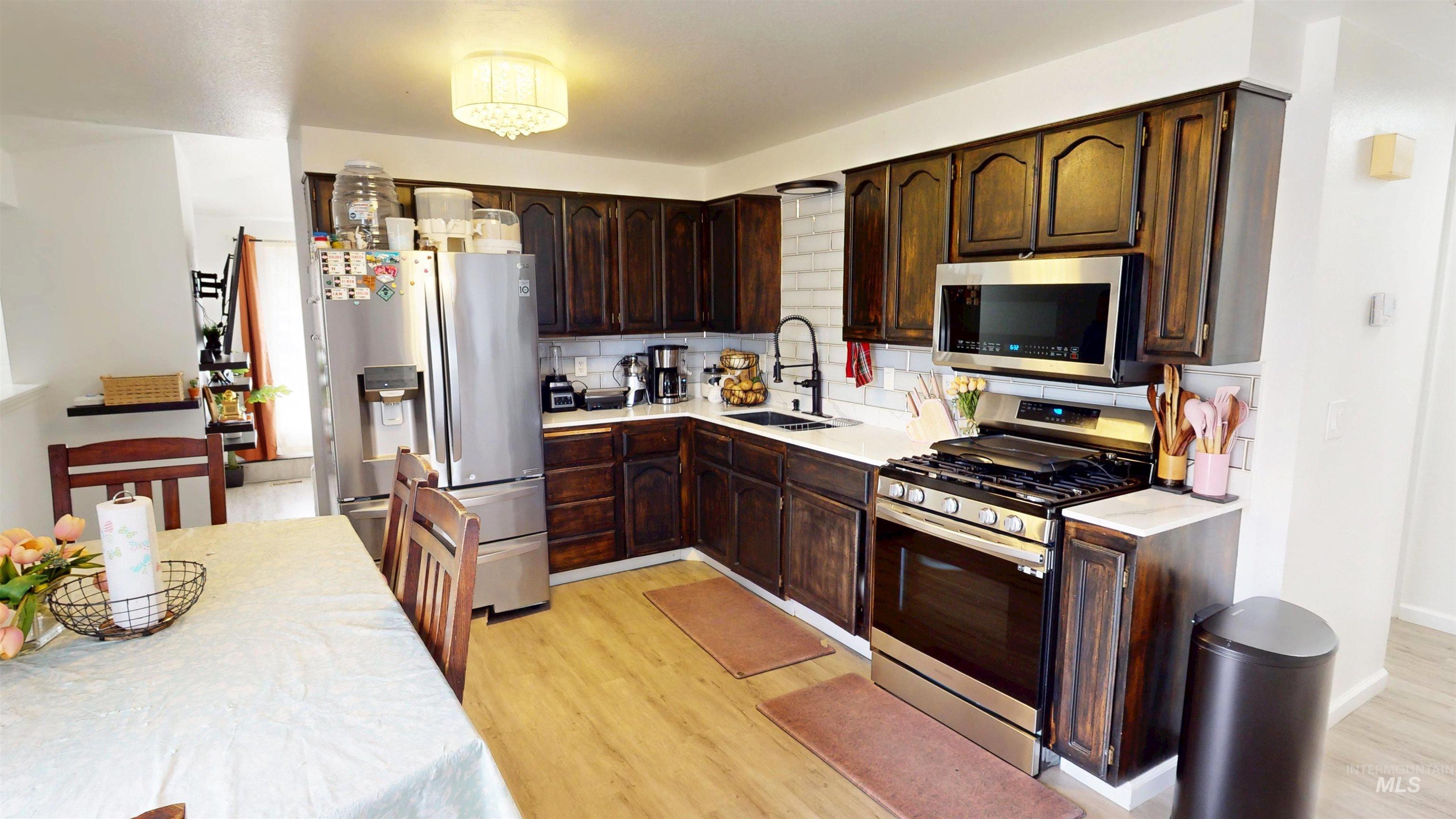 Kitchen featuring appliances with stainless steel finishes, decorative backsplash, dark brown cabinetry, and light wood-style flooring