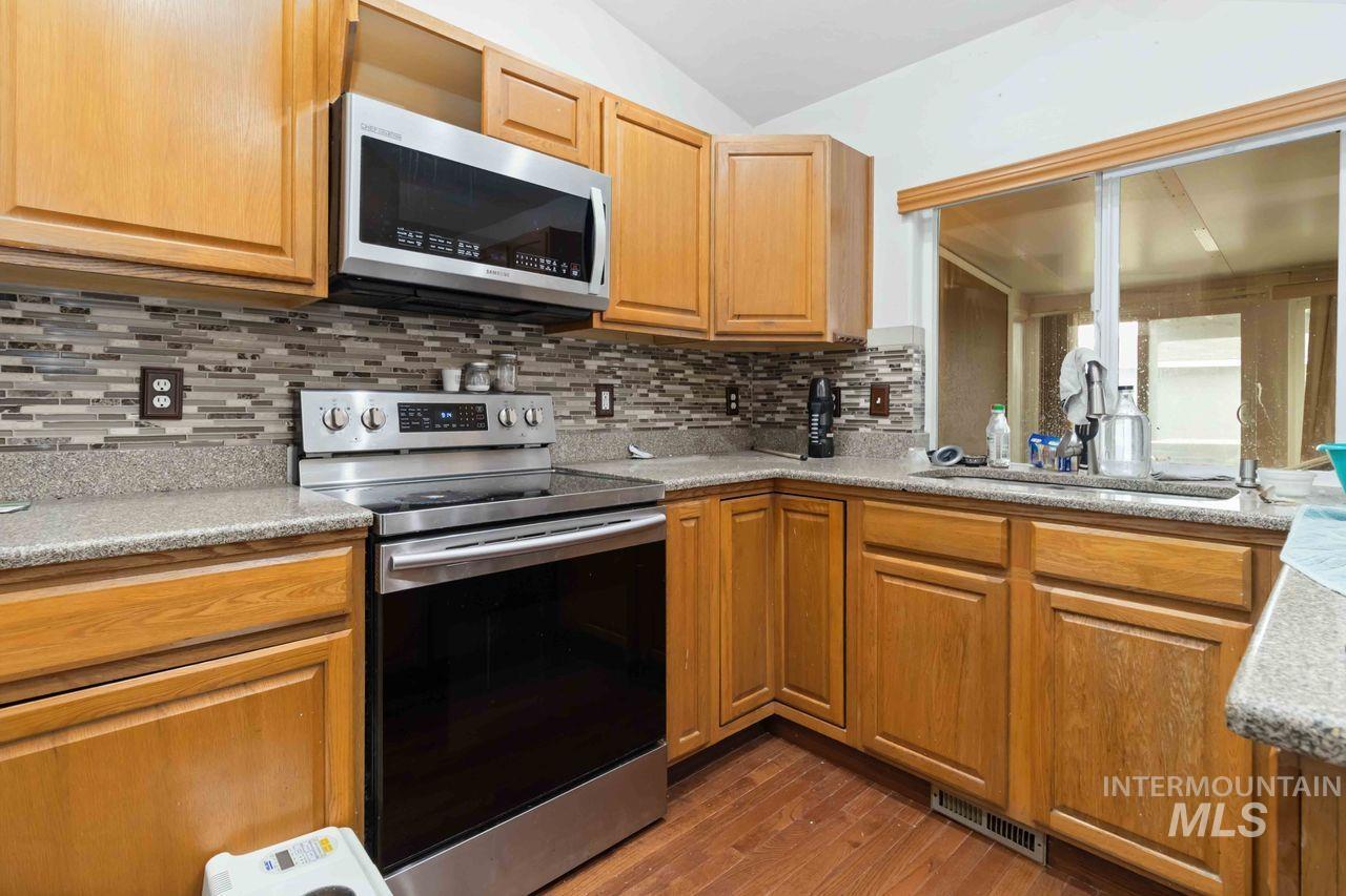 Kitchen featuring stainless steel appliances, dark wood-style flooring, light stone counters, tasteful backsplash, and lofted ceiling