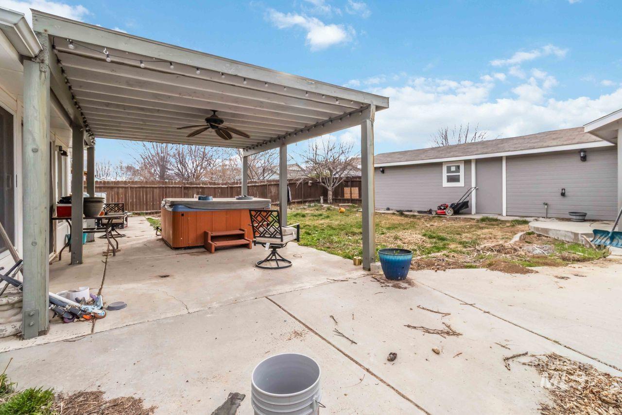 Fenced backyard featuring ceiling fan, a hot tub, and a patio