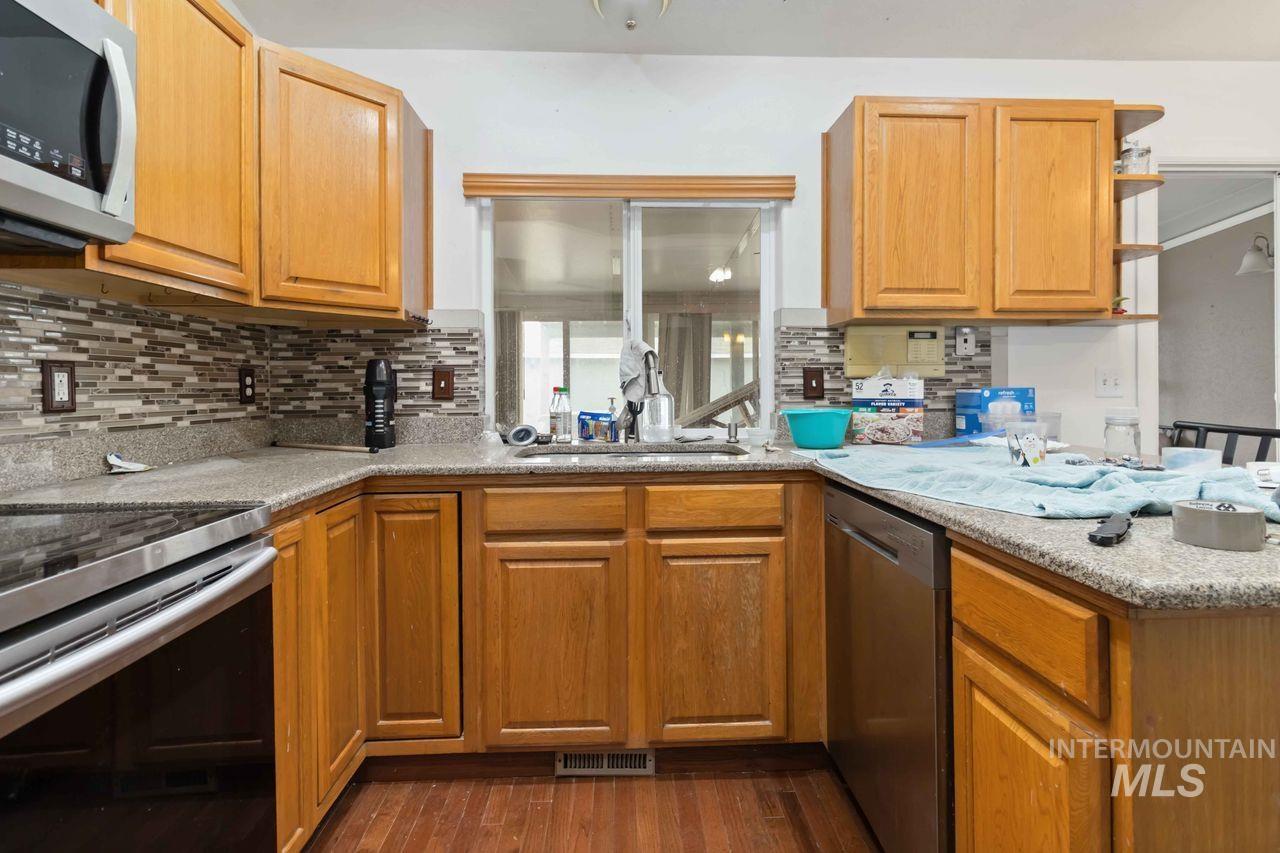 Kitchen with stainless steel appliances, dark wood finished floors, open shelves, light stone counters, and wood finish cabinets