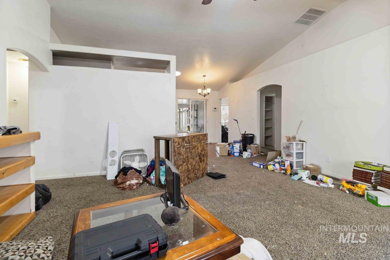Carpeted living area with arched walkways, lofted ceiling, and a chandelier