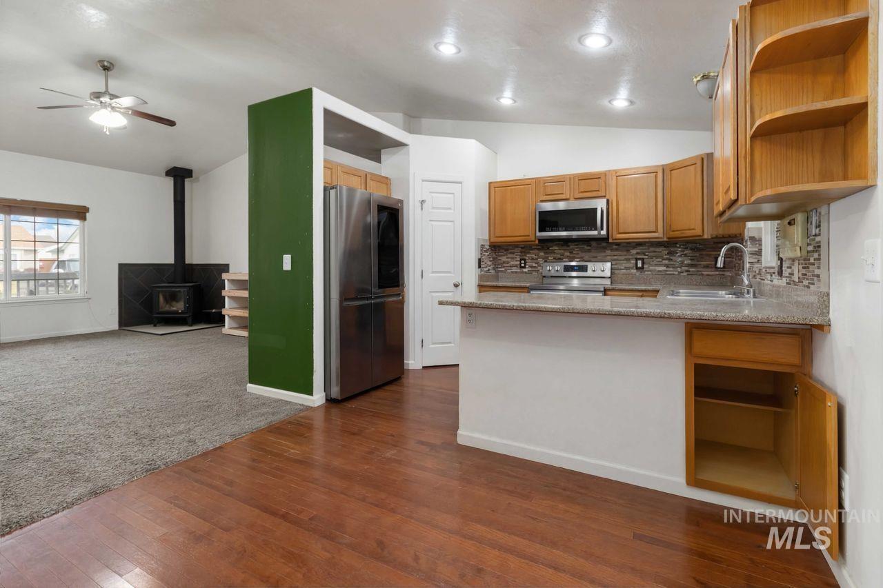 Kitchen featuring open shelves, a peninsula, a wood stove, lofted ceiling, and stainless steel appliances