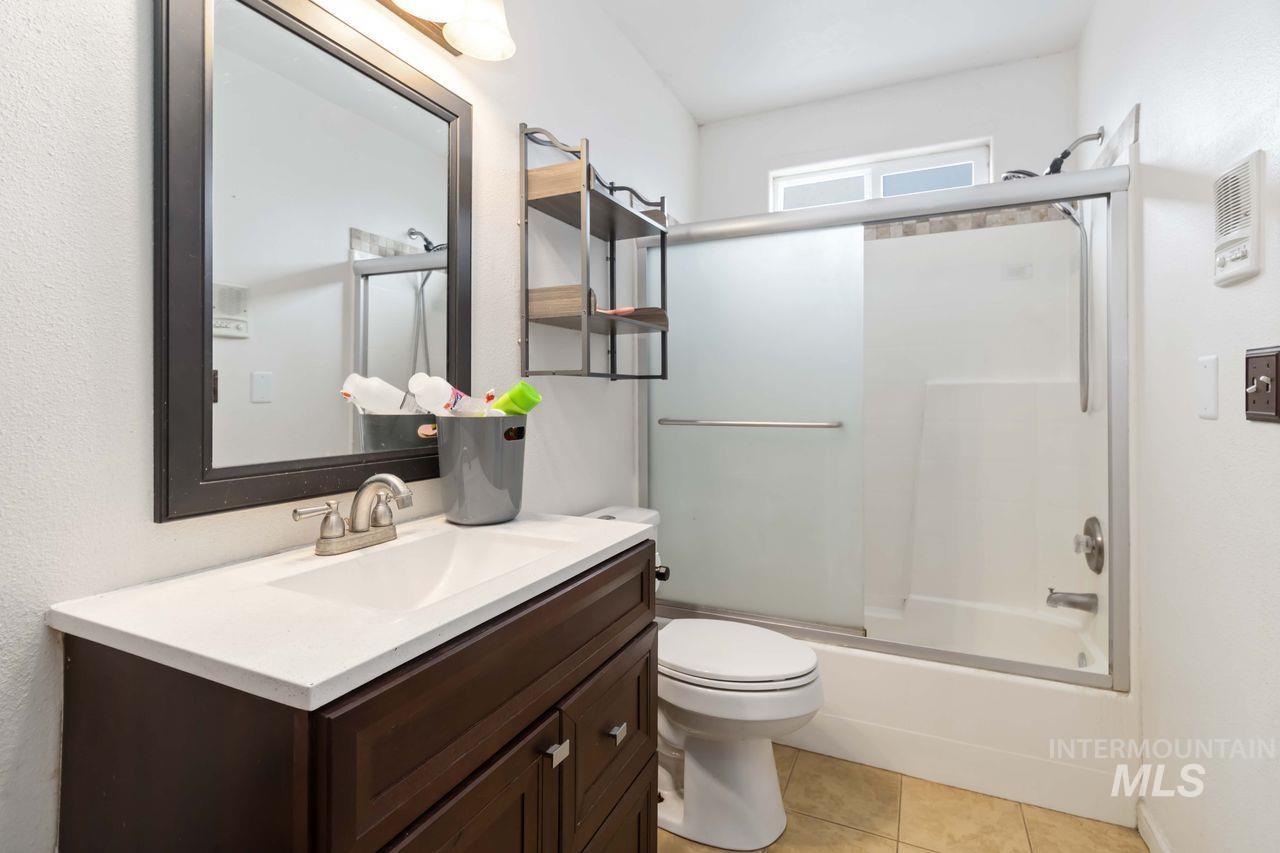 Full bath featuring vanity, enclosed tub / shower combo, light tile patterned flooring, and a textured wall