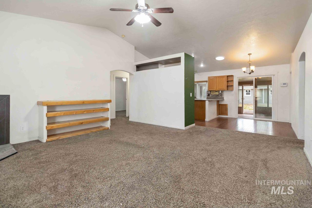 Unfurnished living room with arched walkways, a ceiling fan, dark carpet, lofted ceiling, and suspended lighting