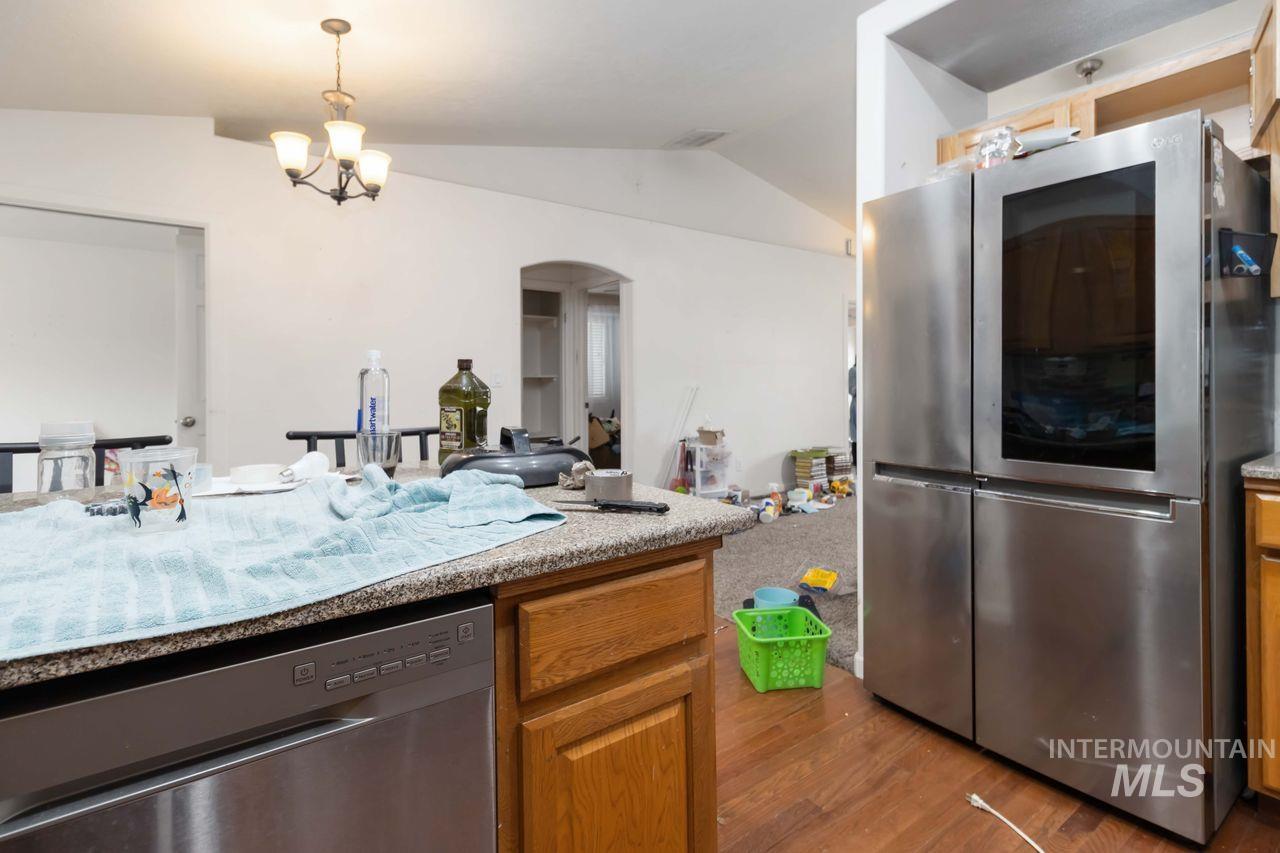 Kitchen featuring stainless steel appliances, lofted ceiling, arched walkways, dark wood finished floors, and wood finish cabinetry