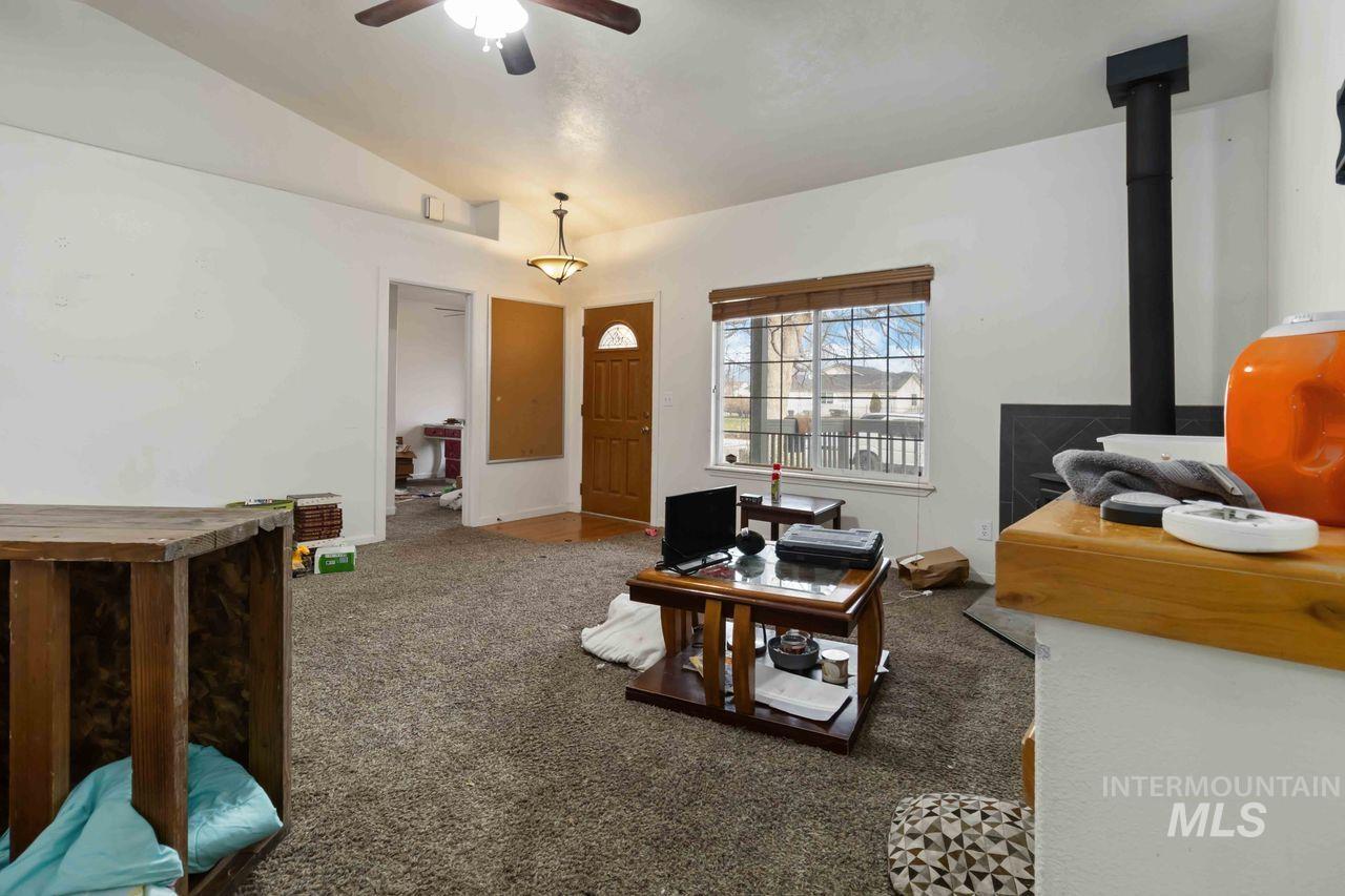 Living room with a wood stove, vaulted ceiling, carpet floors, and a ceiling fan