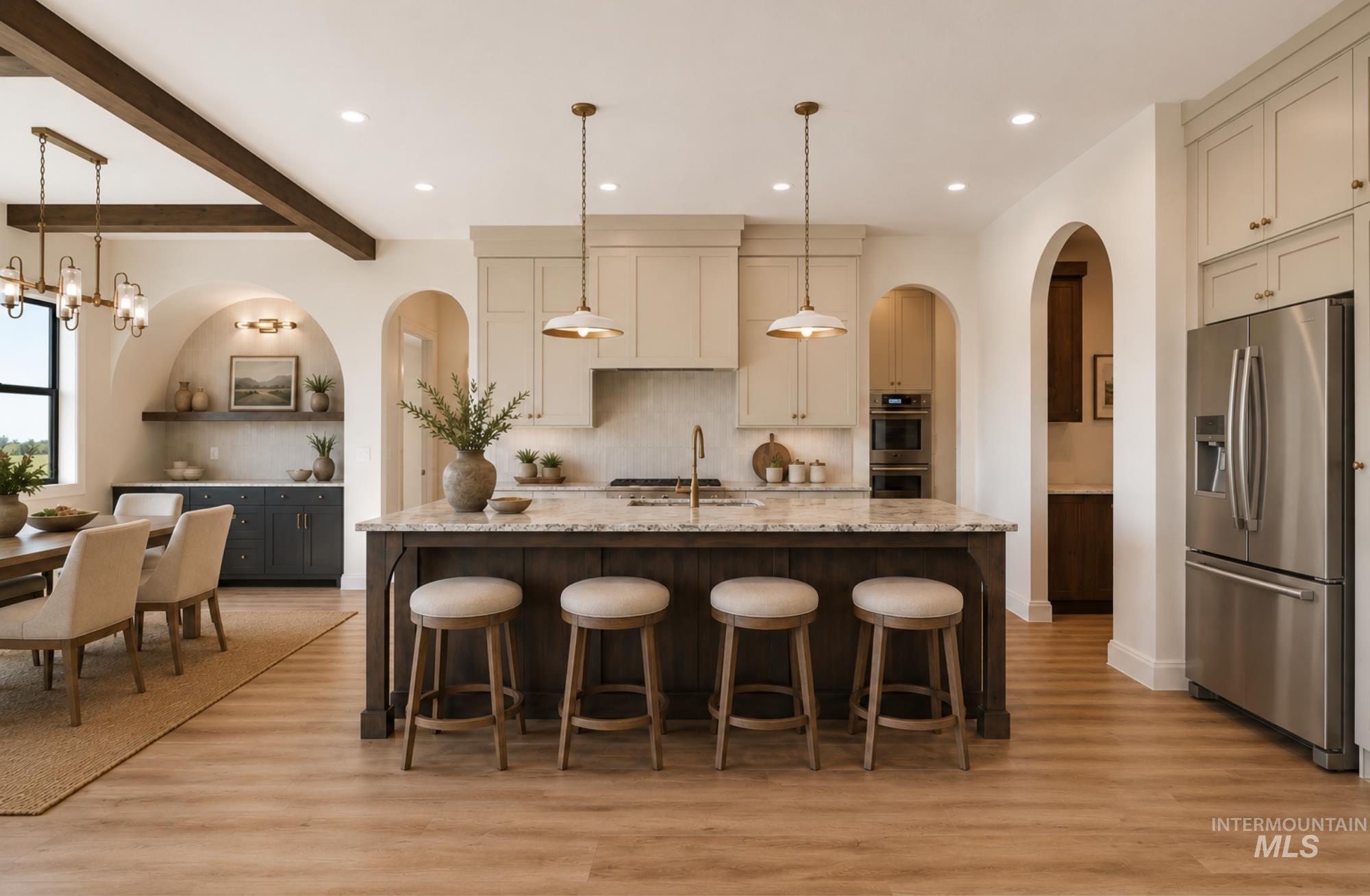 Open-concept kitchen featuring an oversized island with seating, pendant lighting, stainless steel appliances, and wood-finish flooring