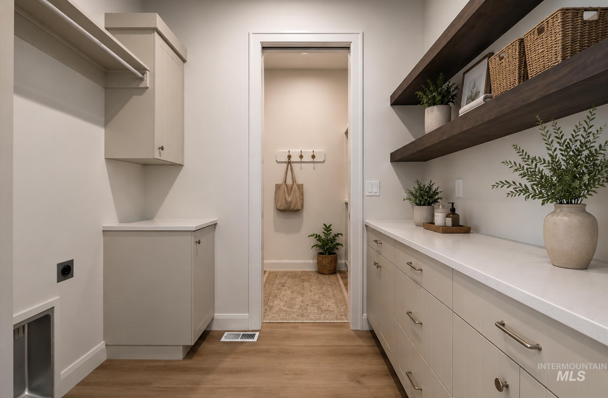 Laundry space with light wood-finish flooring, extensive built-in cabinetry, solid surface countertops, and floating wood shelving