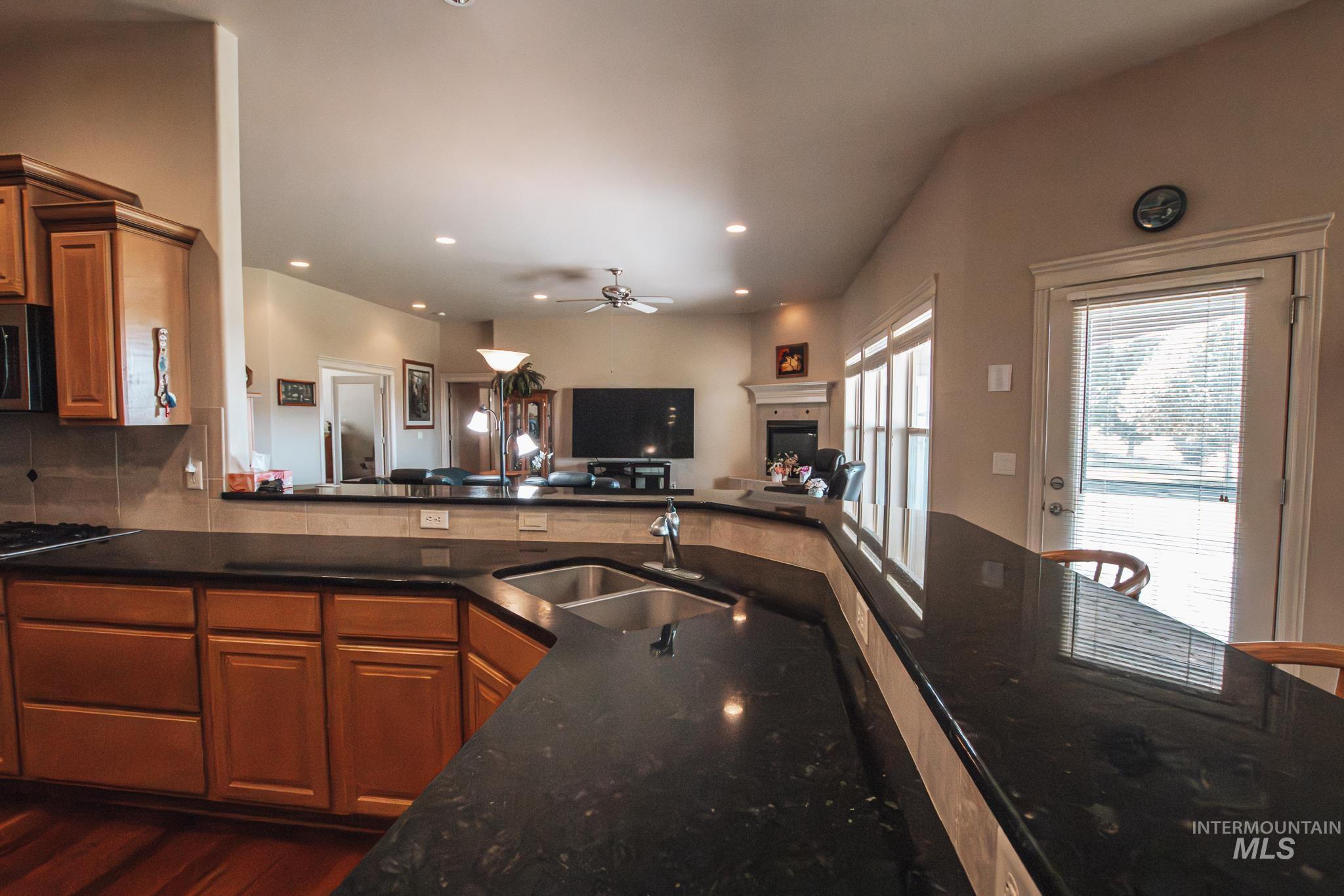 Kitchen featuring brown cabinets, dark stone countertops, open floor plan, ceiling fan, and stainless steel microwave