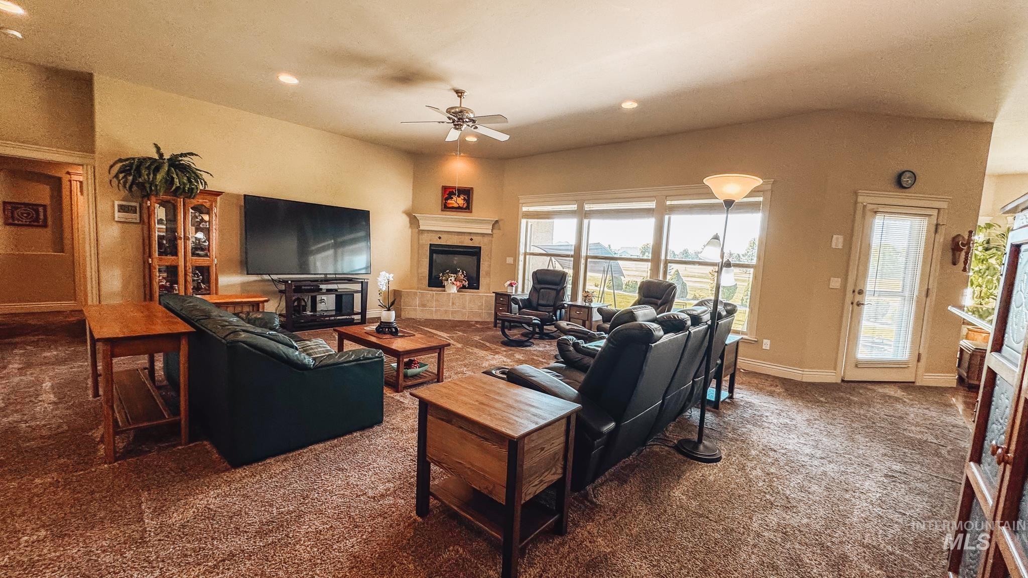 Carpeted living area with a tiled fireplace, a ceiling fan, and recessed lighting