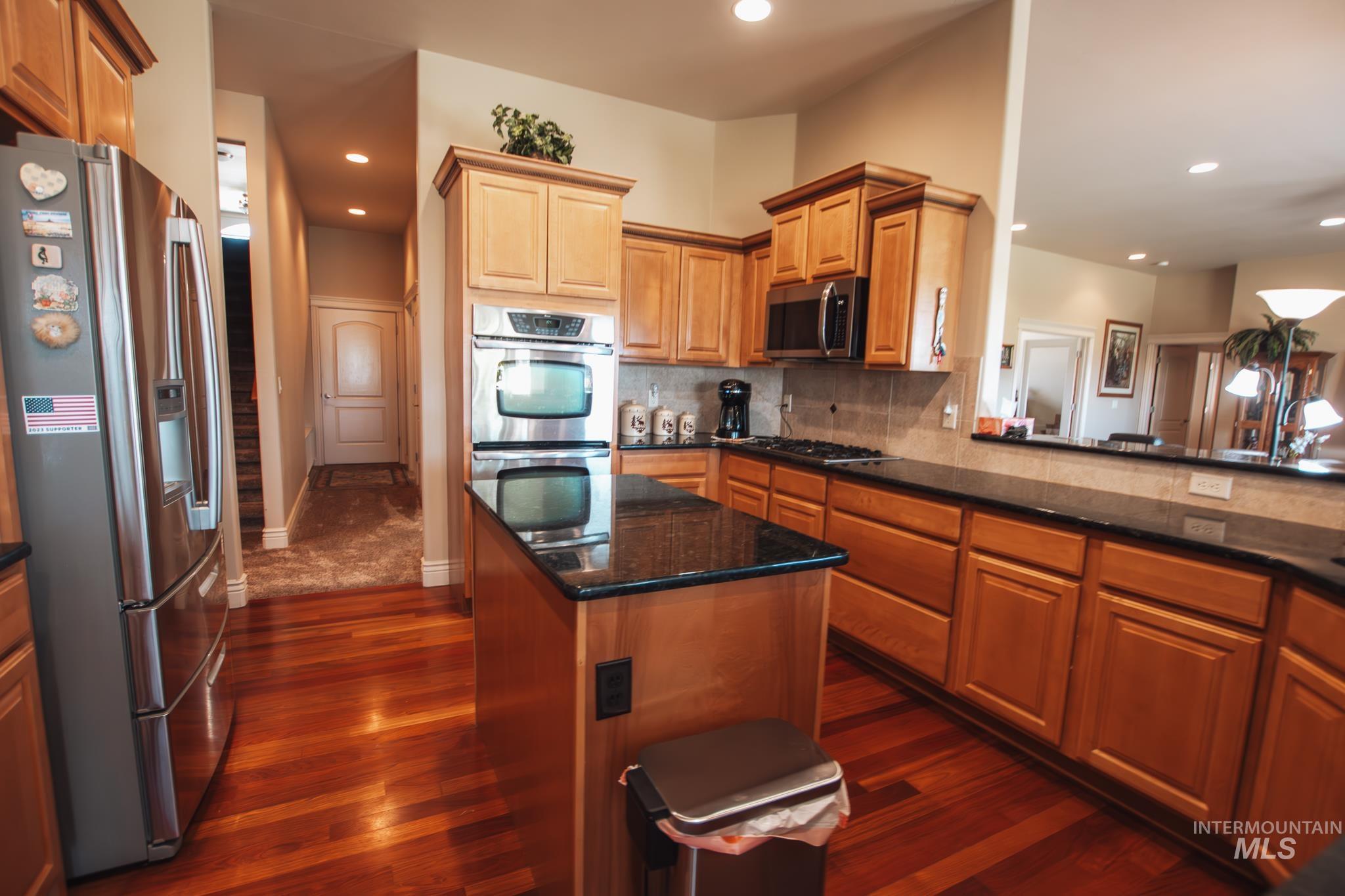 Kitchen featuring stainless steel appliances, tasteful backsplash, dark wood-style floors, recessed lighting, and a kitchen island