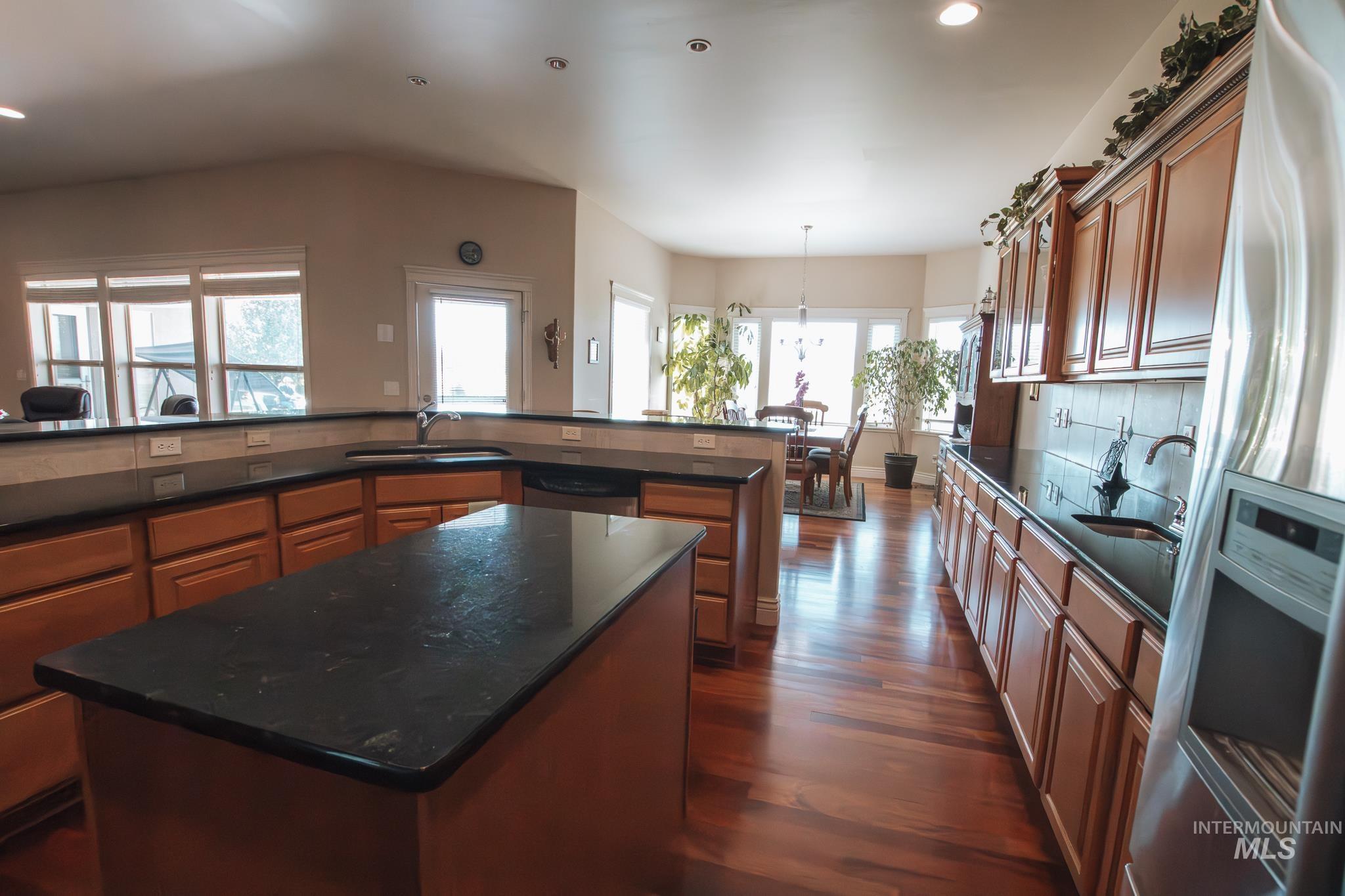 Kitchen with stainless steel appliances, brown cabinets, a center island, recessed lighting, and dark wood-style flooring