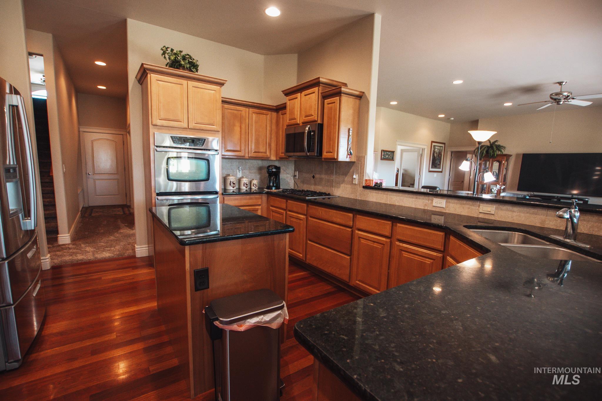 Kitchen with stainless steel appliances, tasteful backsplash, dark wood finished floors, recessed lighting, and dark stone countertops
