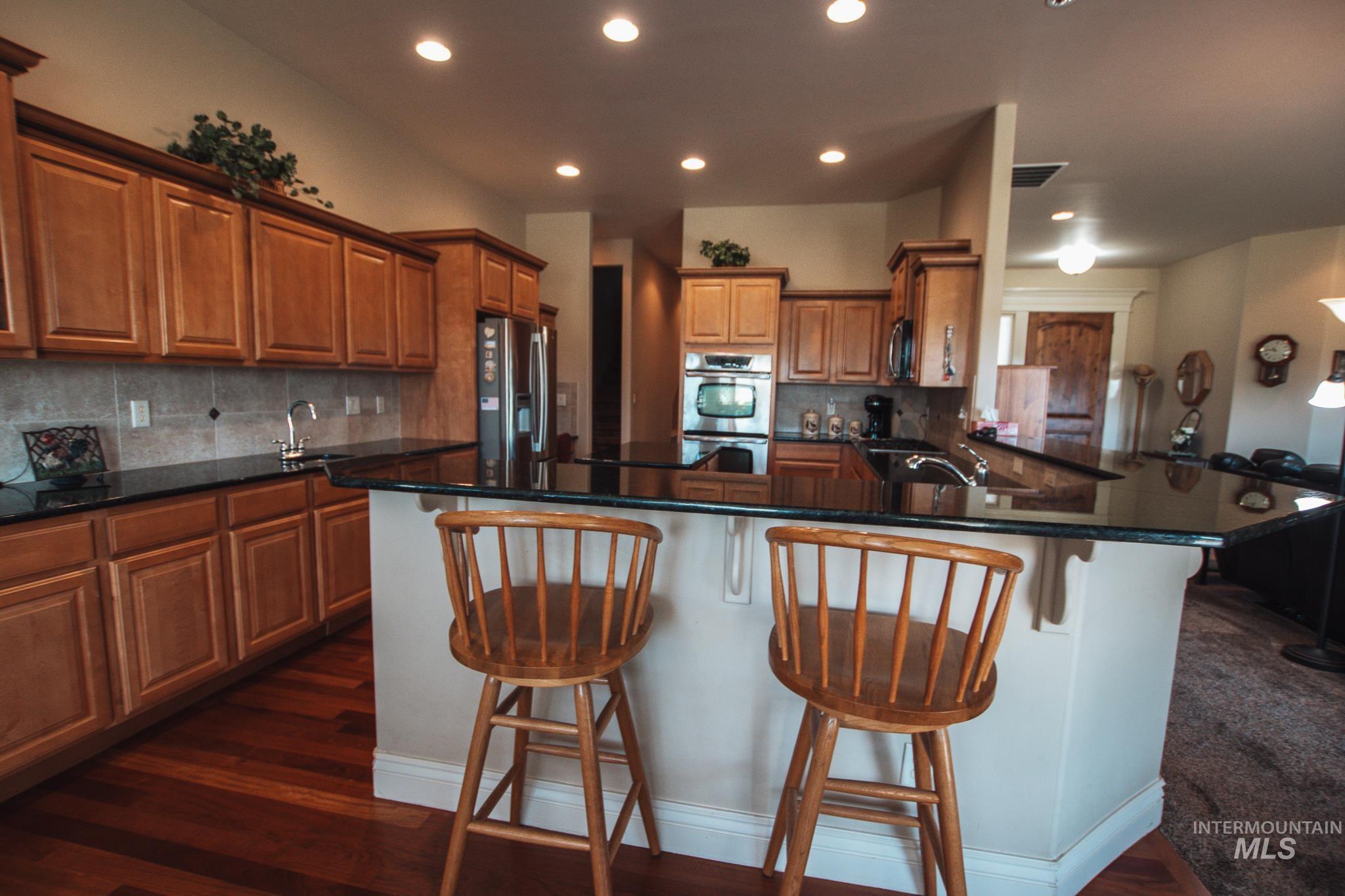 Kitchen with breakfast bar, a peninsula brown cabinetry, appliances with stainless steel finishes, and recessed lighting