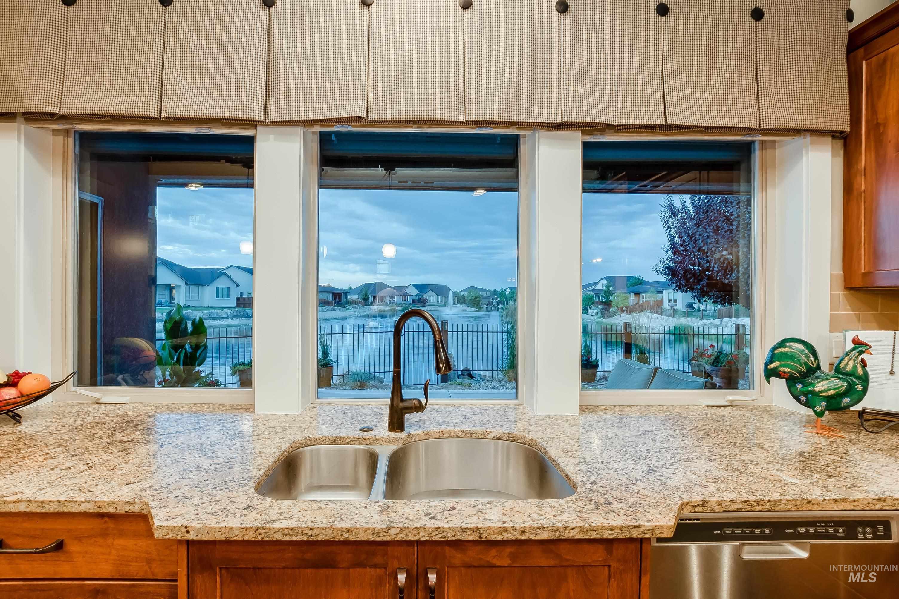 Kitchen featuring brown cabinets, a residential view, dishwasher, and light stone countertops