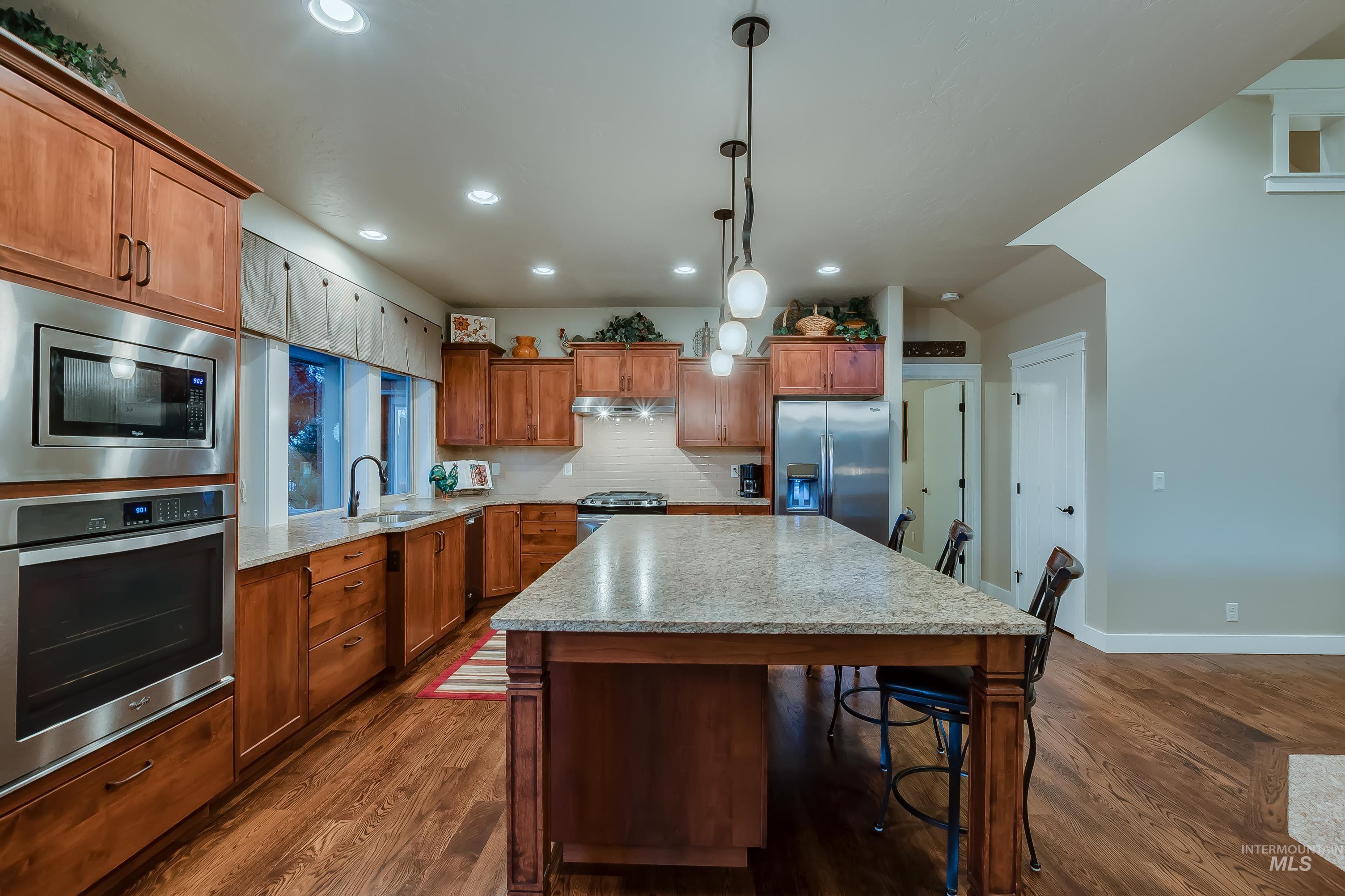 Kitchen featuring a kitchen bar, stainless steel appliances, dark wood-style floors, hanging light fixtures, and brown cabinets