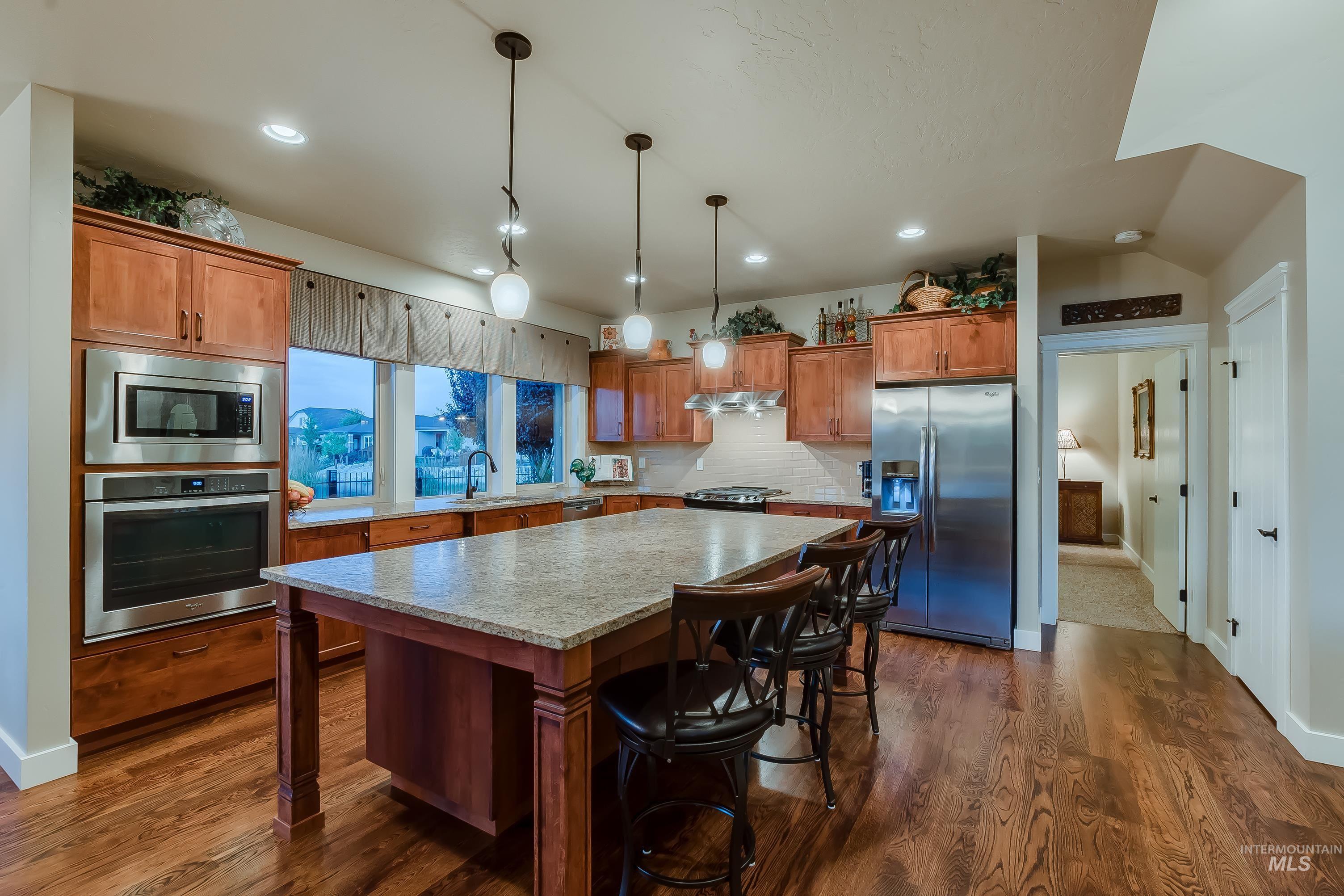 Kitchen with appliances with stainless steel finishes, a breakfast bar, a kitchen island, brown cabinets, and dark wood-type flooring
