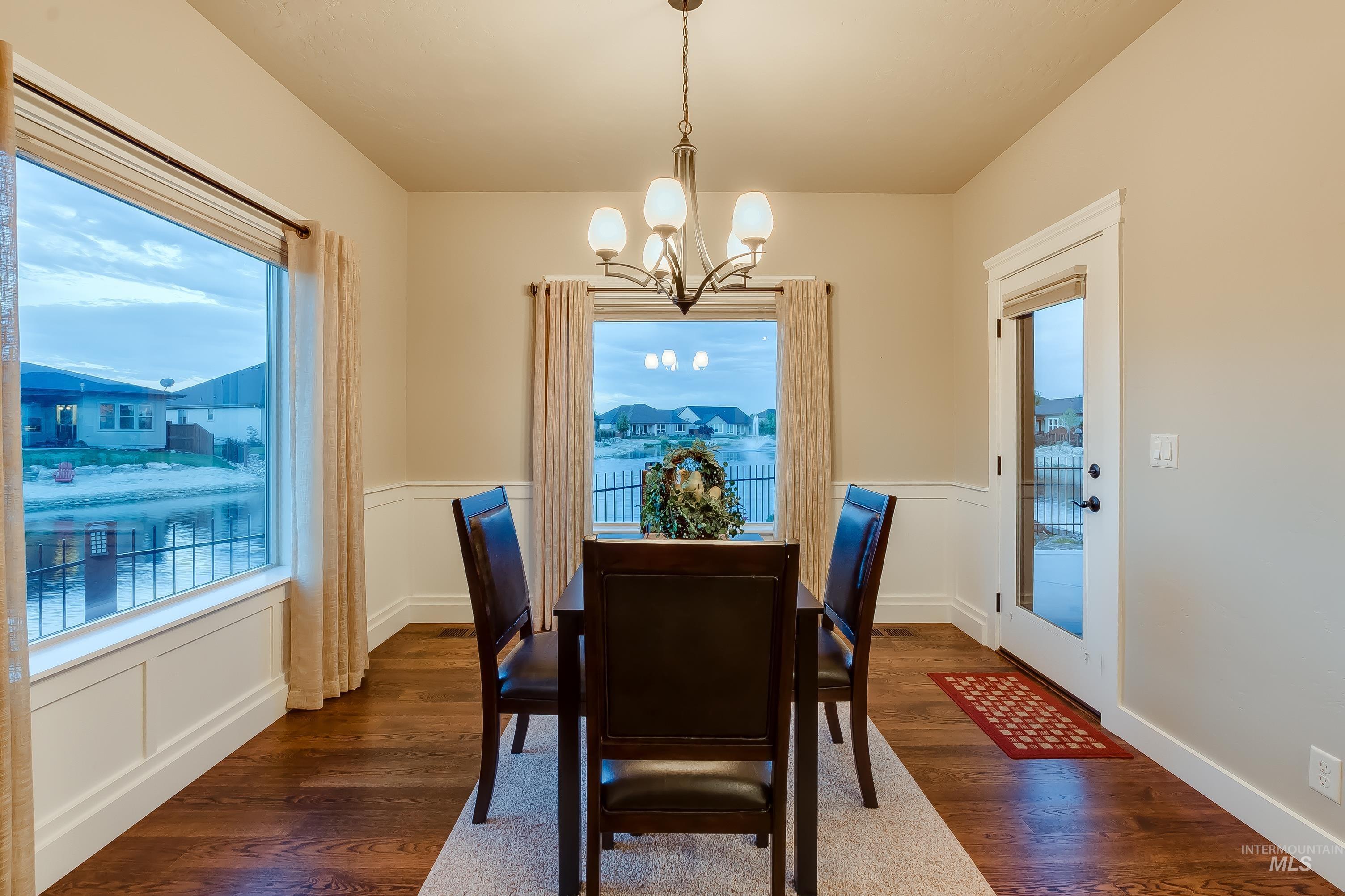 Dining room featuring healthy amount of natural light, dark wood-style flooring, wainscoting, and a chandelier