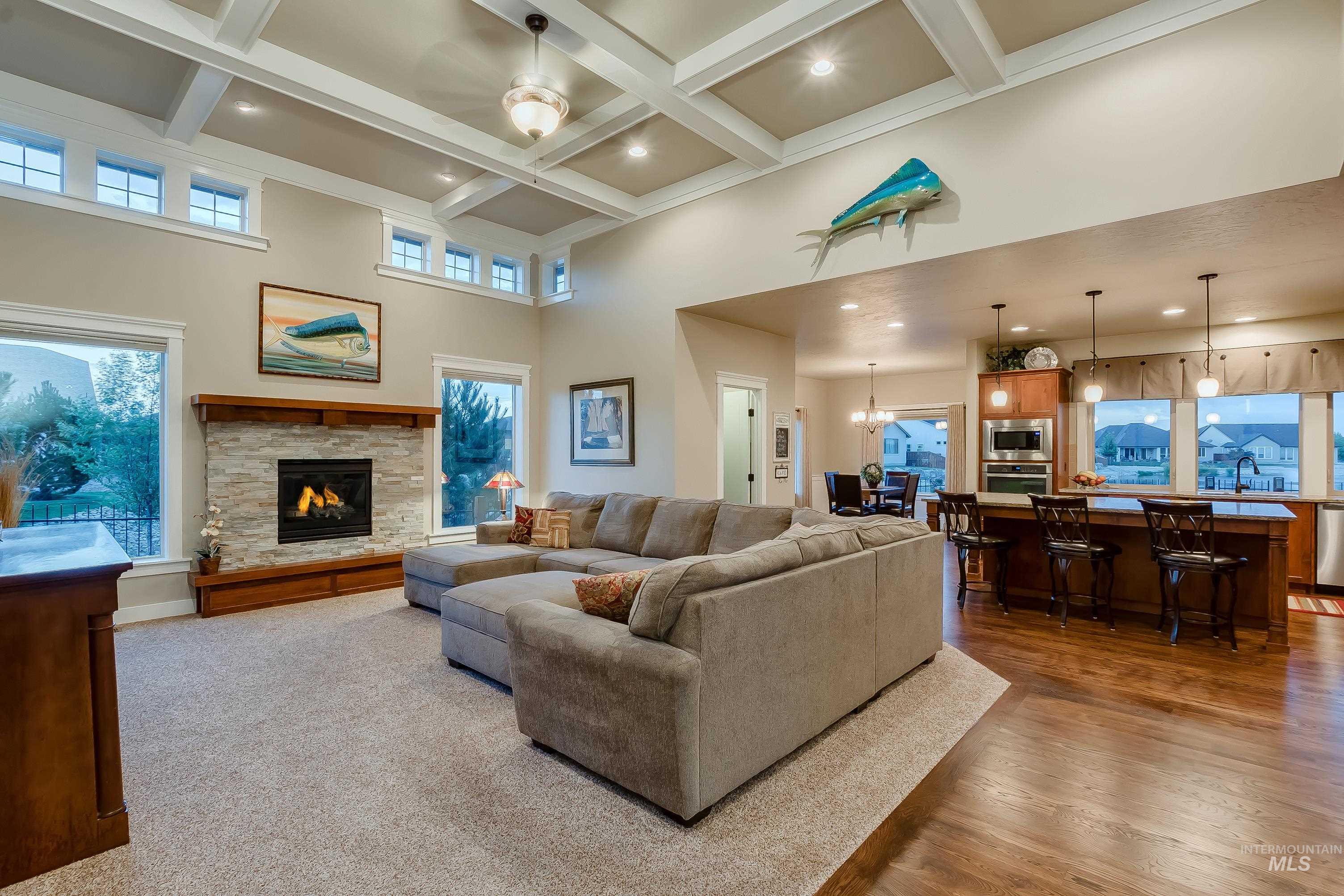 Living room with beam ceiling, a high ceiling, a stone fireplace, a chandelier, and coffered ceiling