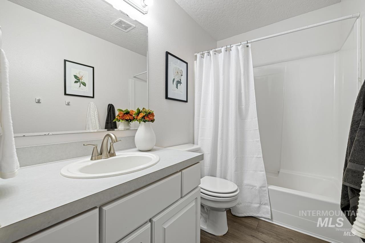 Bathroom featuring vanity, wood finished floors, a textured ceiling, and shower / bath combination with curtain