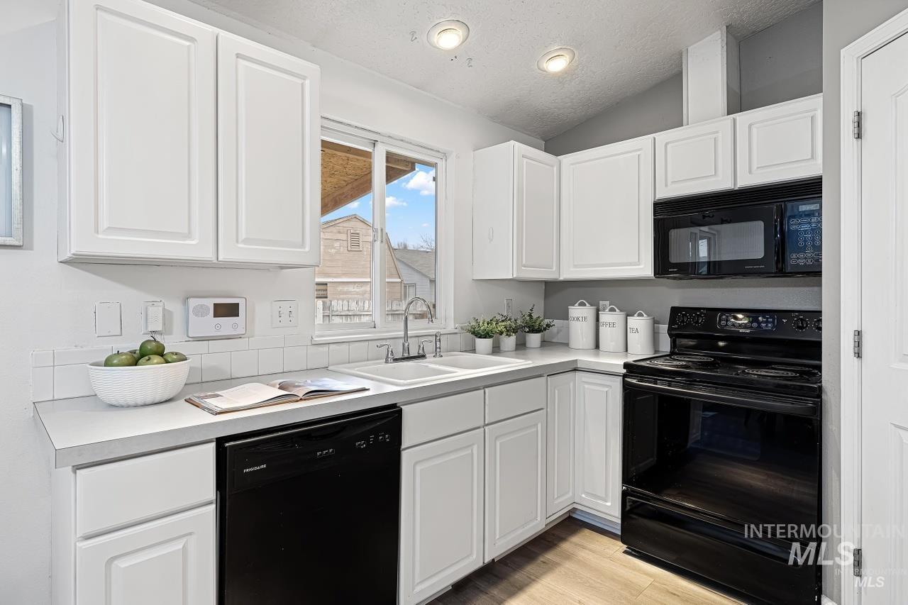 Kitchen featuring black appliances, lofted ceiling, white cabinets, light countertops, and light wood-style flooring