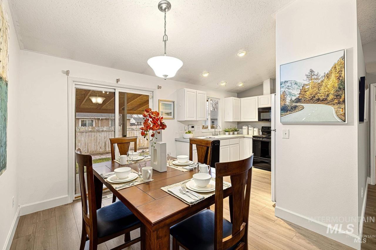 Dining area with a textured ceiling, light wood-style floors, and vaulted ceiling