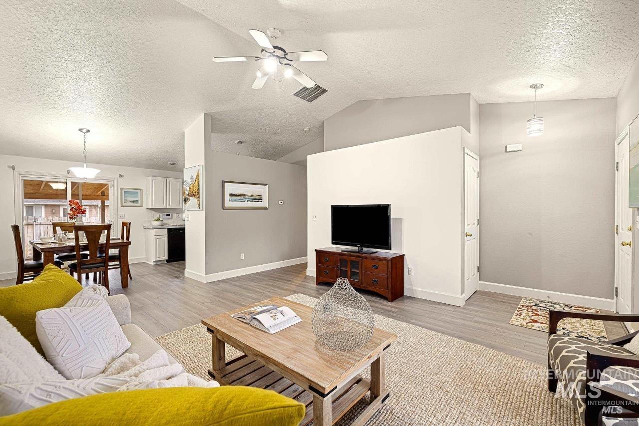 Living room featuring ceiling fan, light wood-style flooring, a textured ceiling, and lofted ceiling