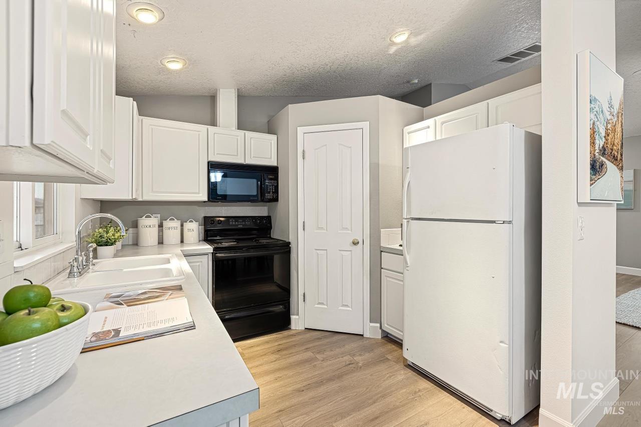 Kitchen with black appliances, white cabinetry, light countertops, light wood-type flooring, and a textured ceiling