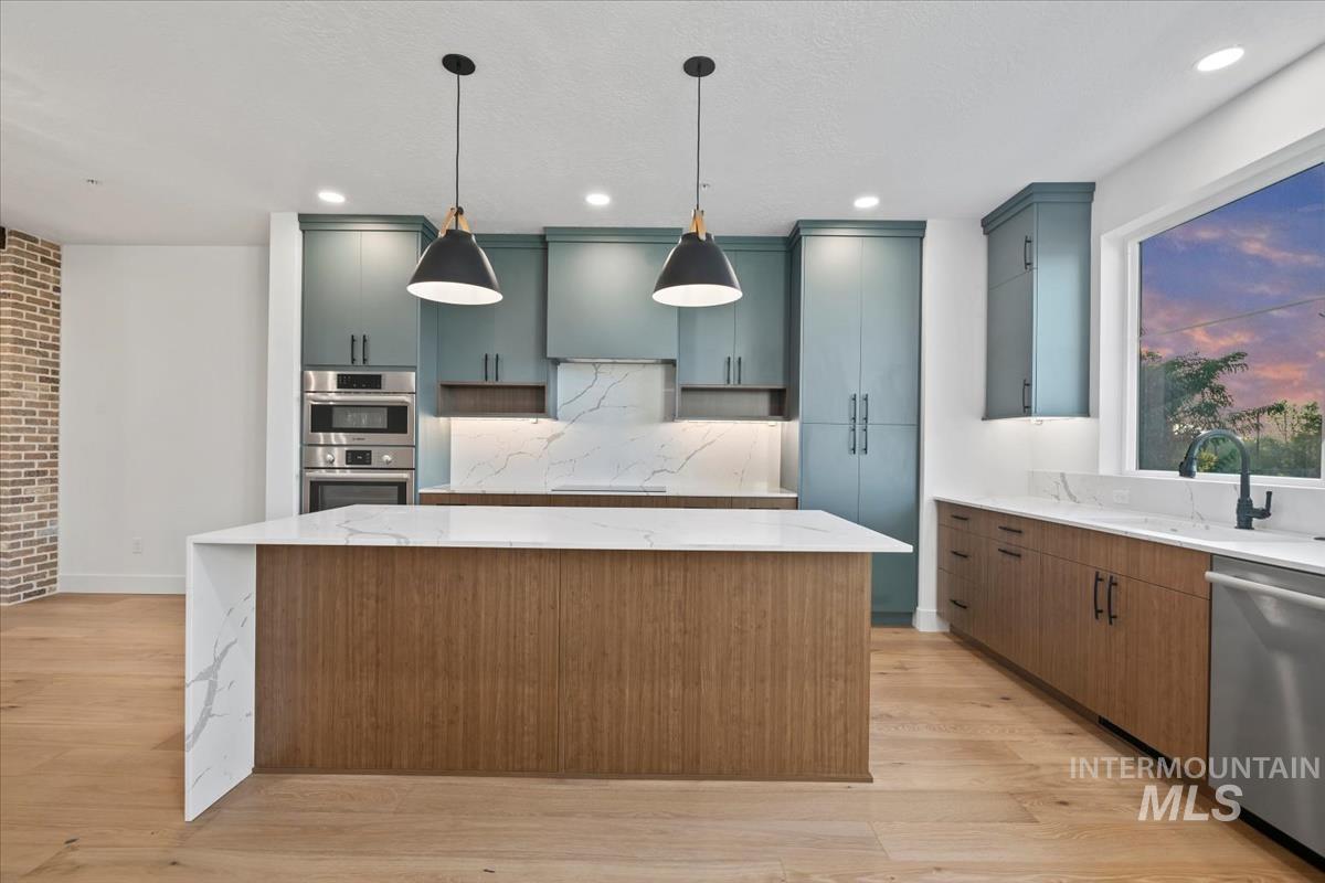 Kitchen featuring stainless steel appliances, light stone countertops, a center island, hanging light fixtures, and light wood-style flooring