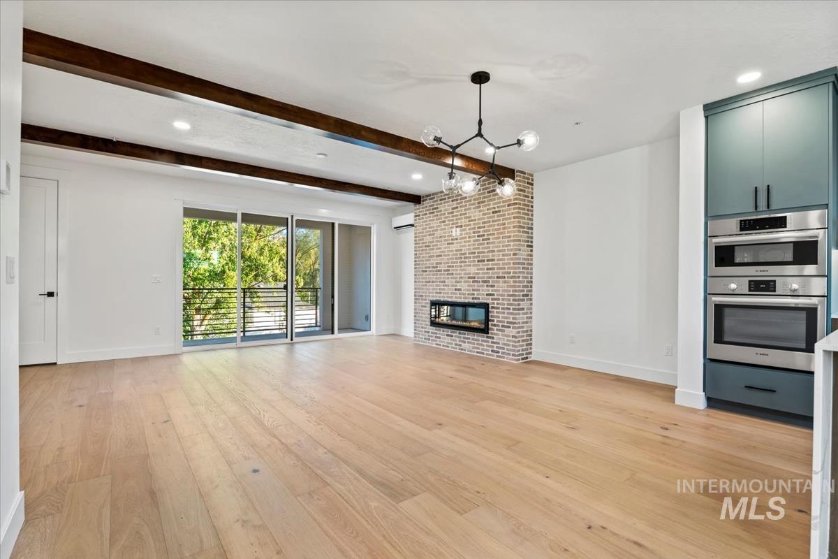 Unfurnished living room featuring light wood-style flooring, beam ceiling, a large fireplace, recessed lighting, and a chandelier