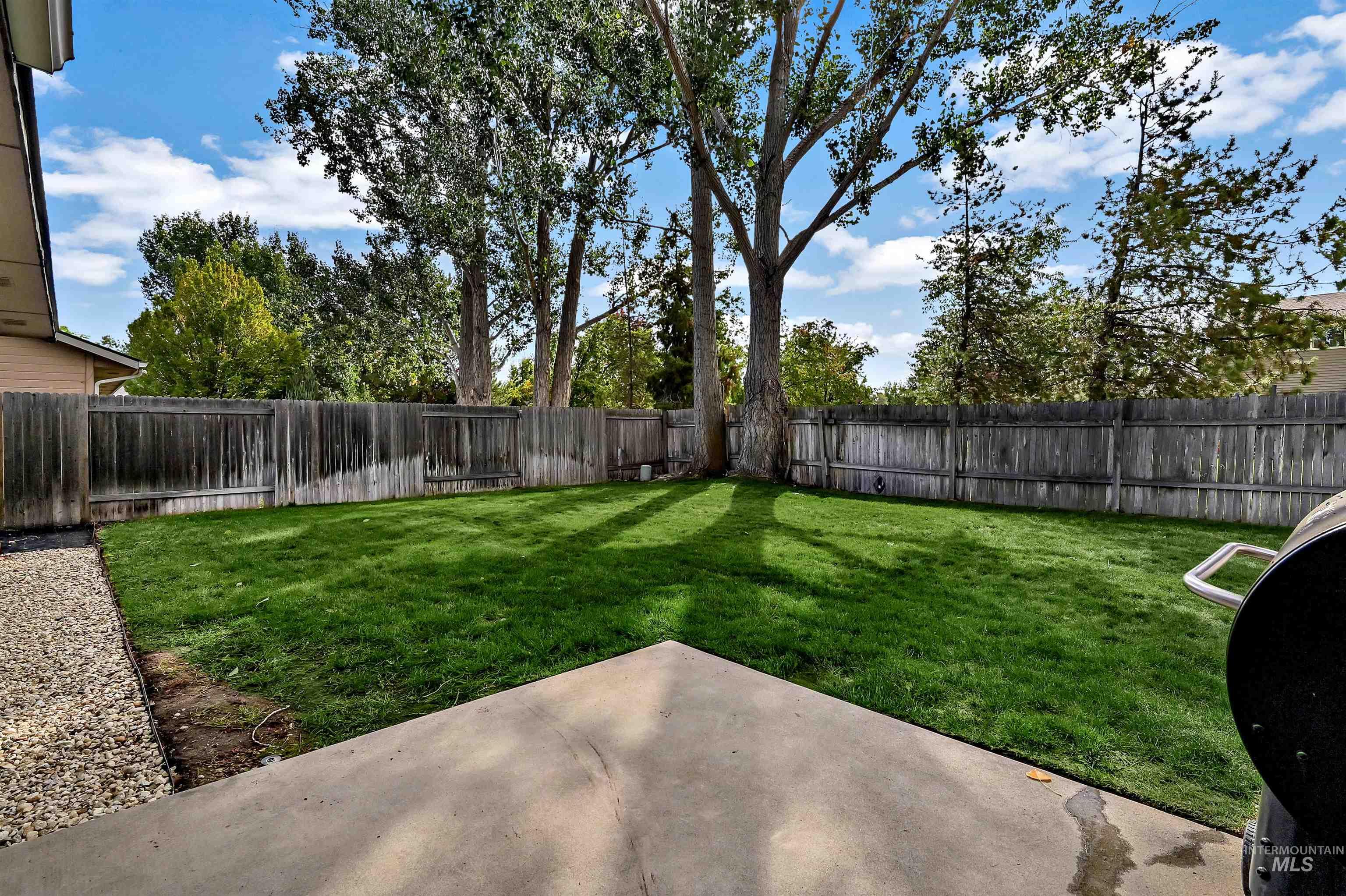 Large fenced backyard featuring a concrete patio area & mature trees