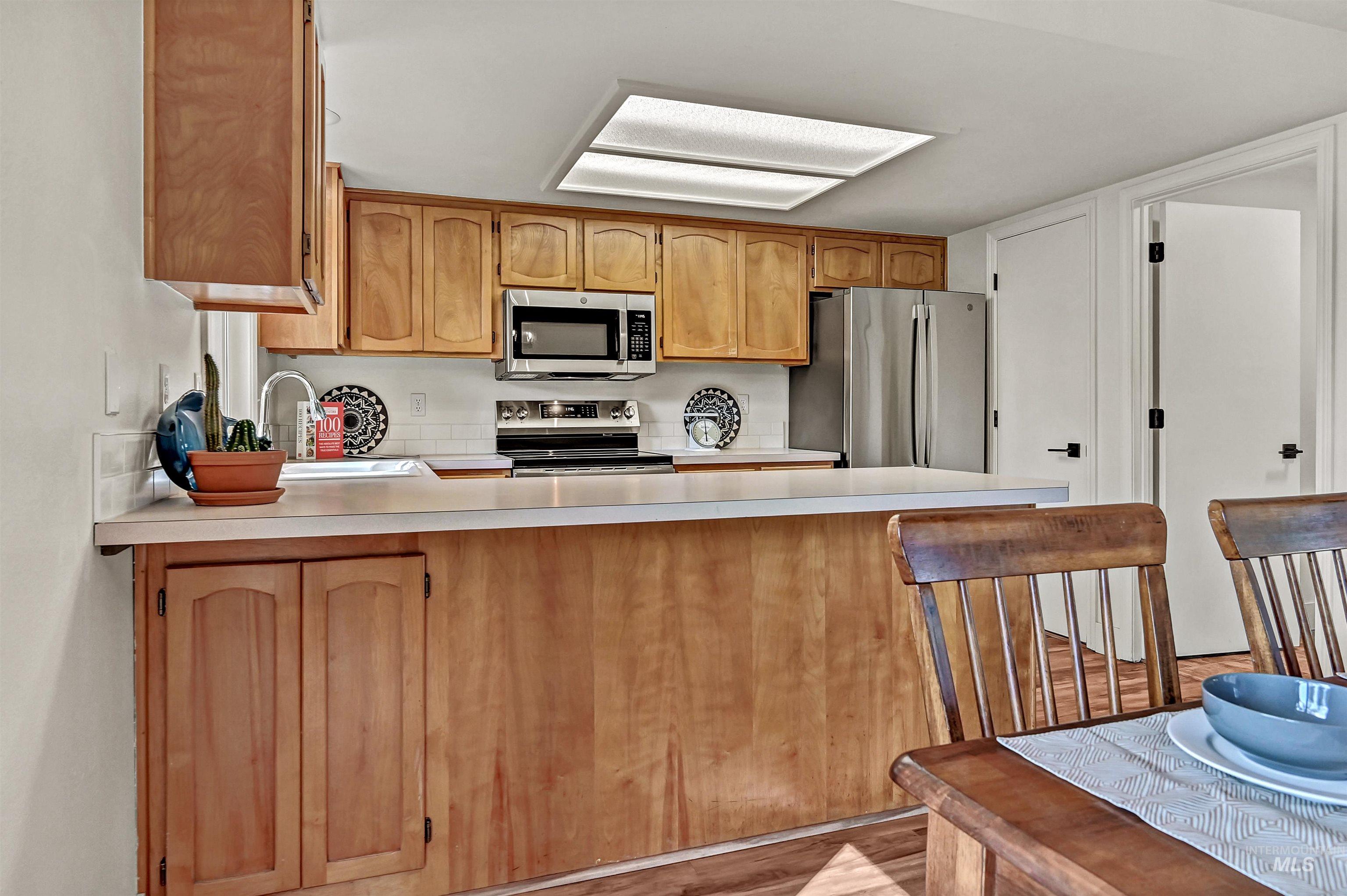 Kitchen with light countertops, stainless steel appliances, a peninsula, and light wood-style floors