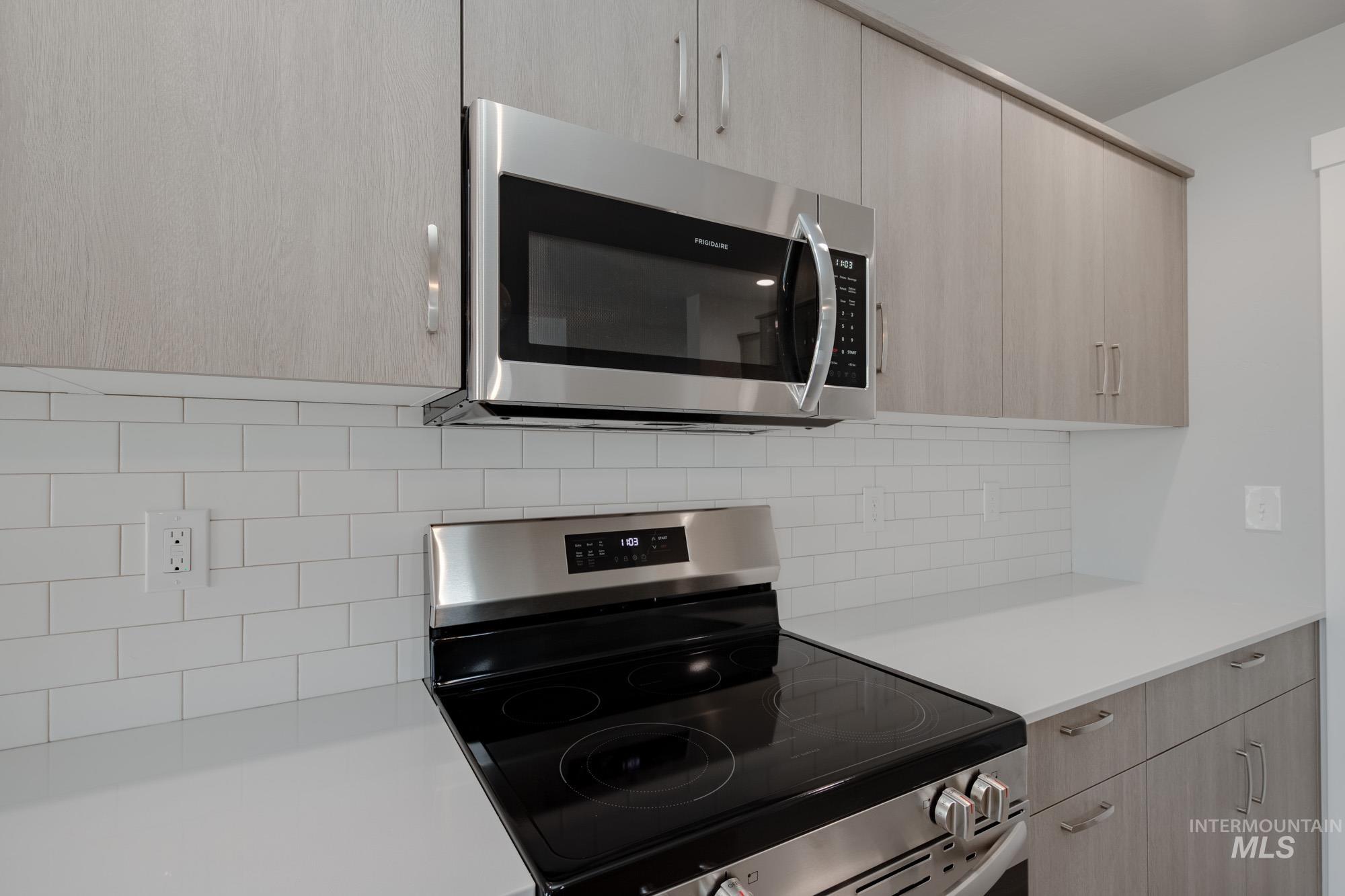 Kitchen with appliances with stainless steel finishes, light brown cabinetry, modern cabinets, and backsplash