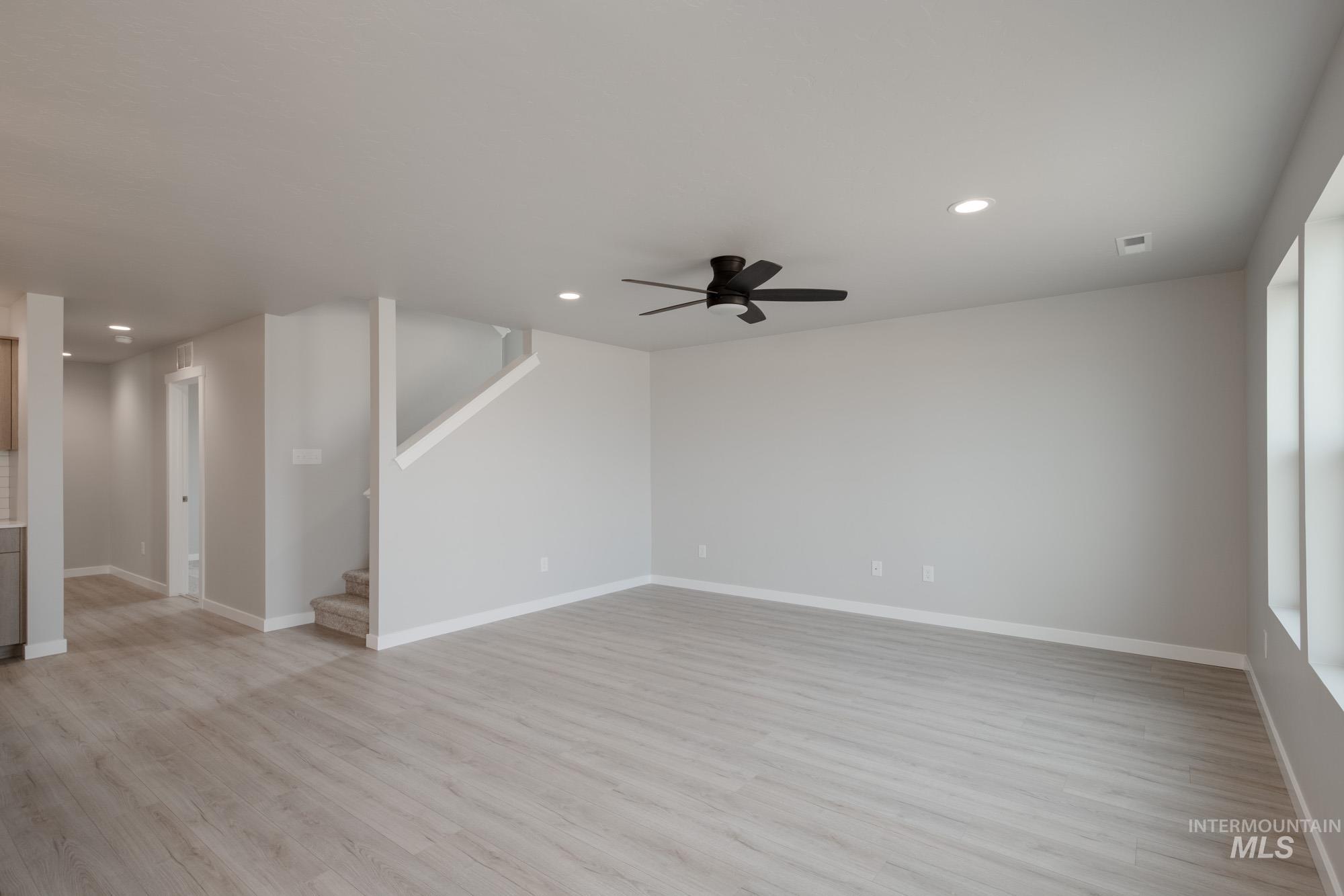 Unfurnished living room with light wood-style floors, ceiling fan, recessed lighting, and stairway