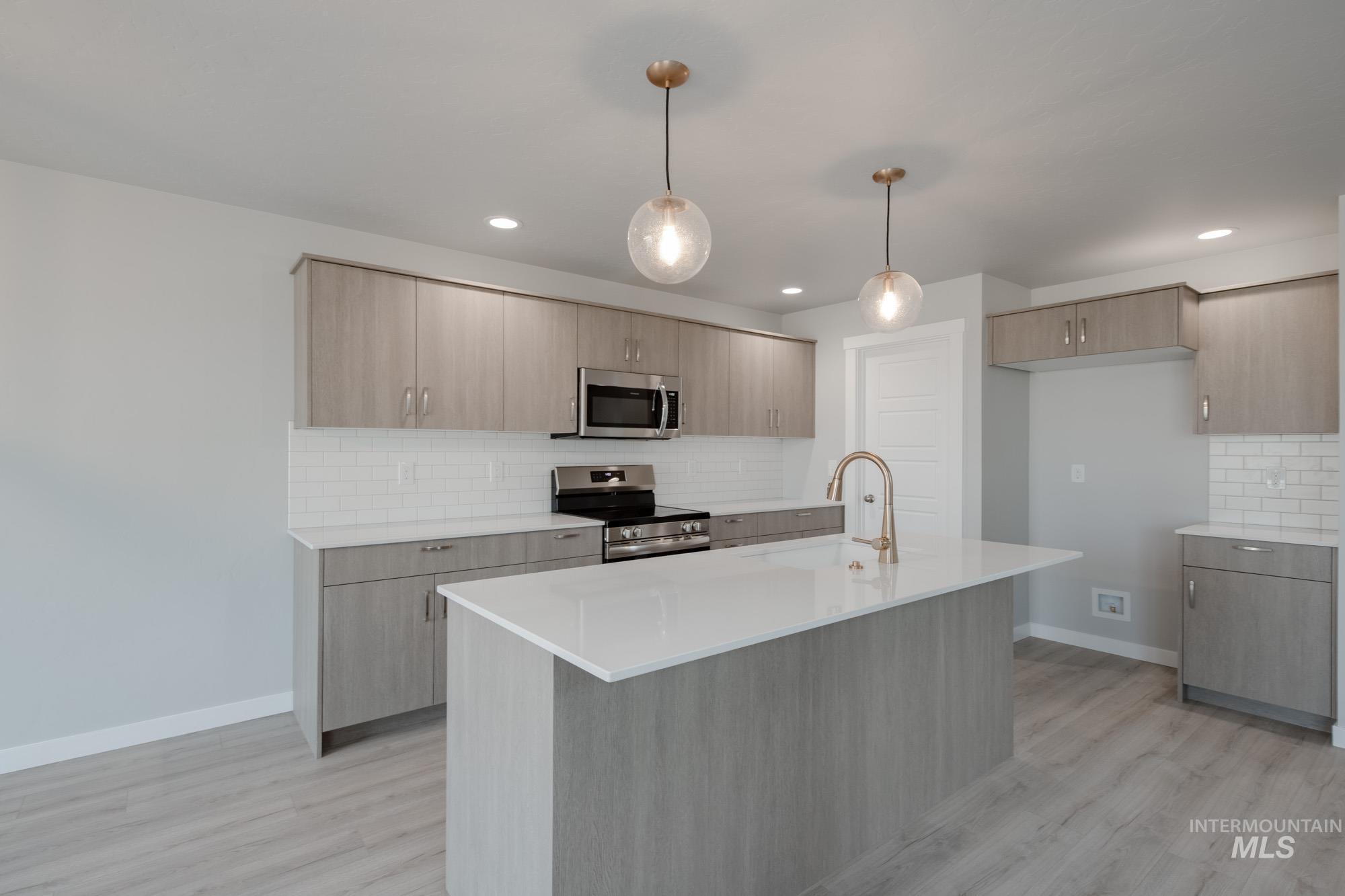 Kitchen featuring backsplash, appliances with stainless steel finishes, pendant lighting, light stone counters, and light wood-style flooring