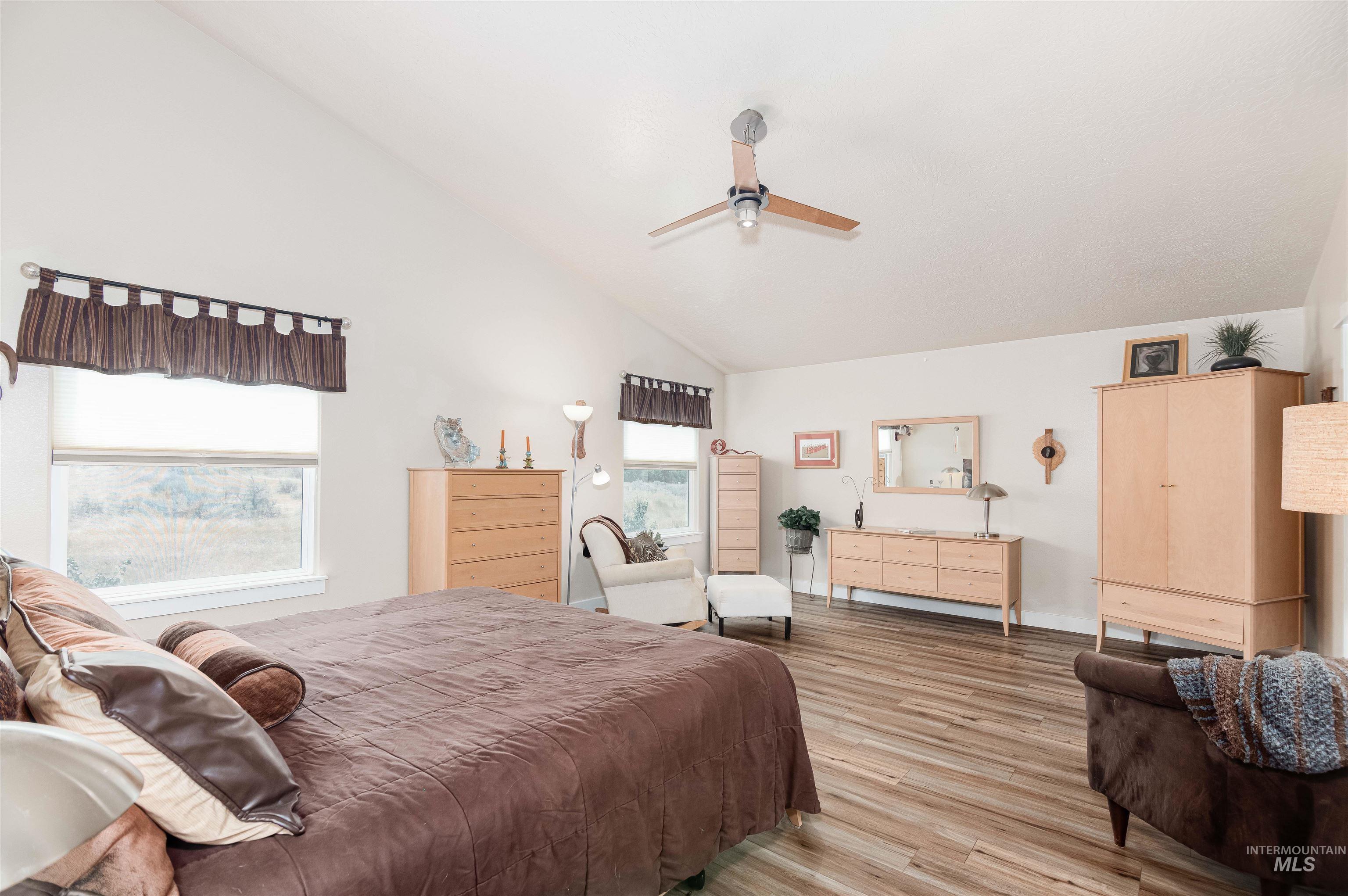 Vaulted ceilings with a ceiling fan, wood-finish flooring, and multiple windows providing natural light